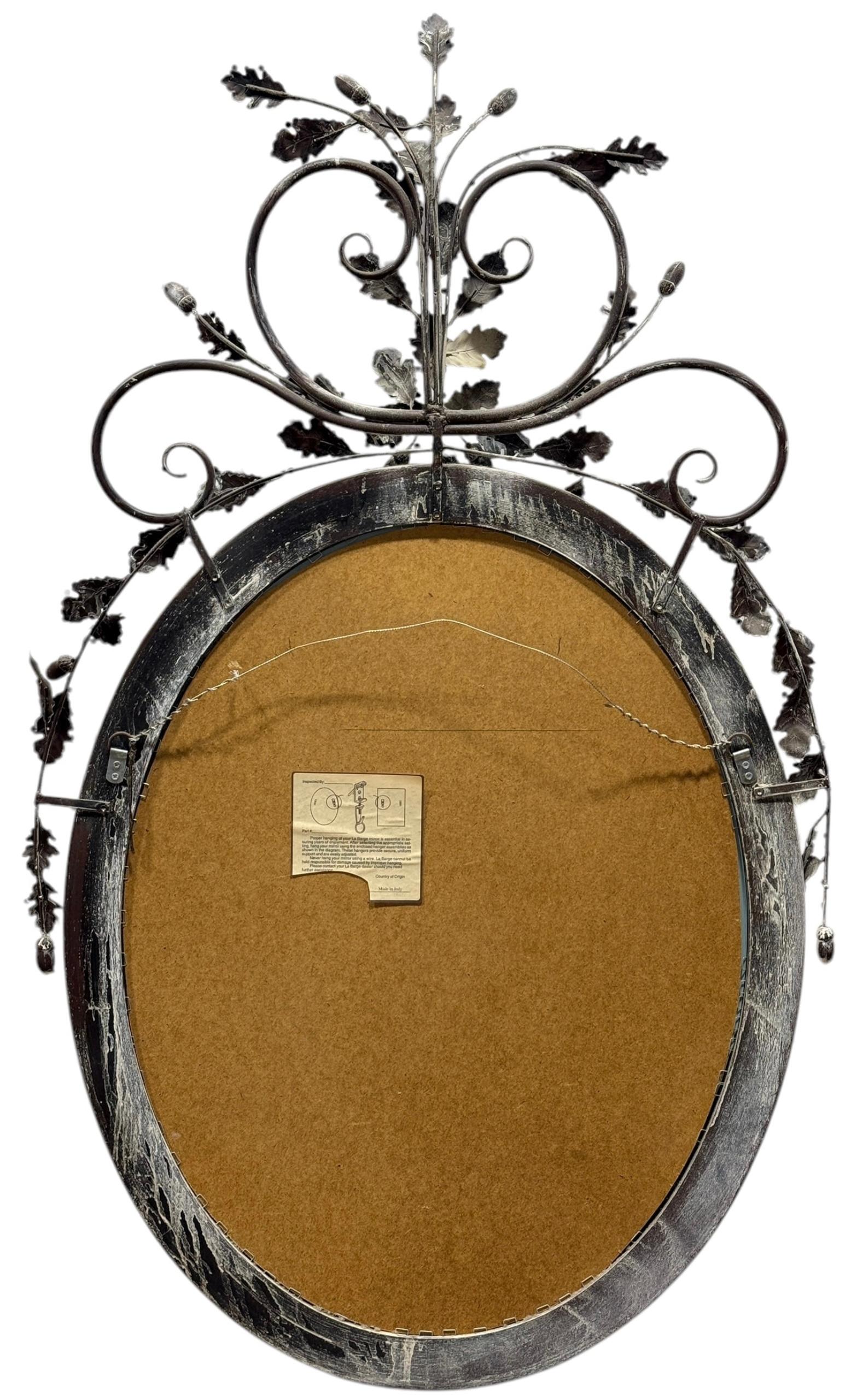 This is a mid-century tole and wood mirror by LaBarge. The oval frame is a distressed gilt and brown wood. The maple leaf and acorn tole are also brown with green and white accents, it is marked.