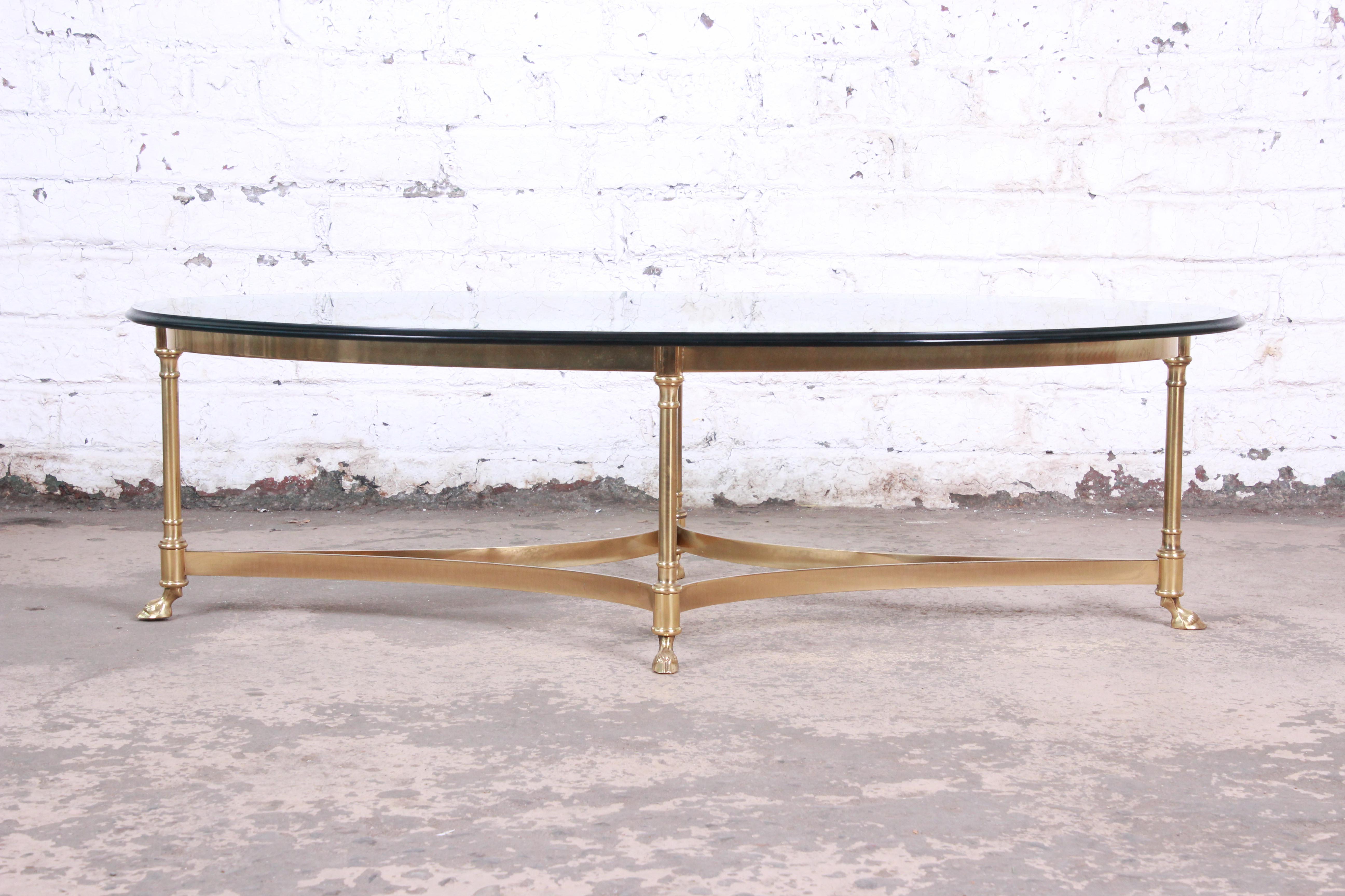 A gorgeous midcentury Hollywood Regency brass and glass coffee or cocktail table by Labarge. The table features a stylish brass base with curved stretchers and unique hooved feet. The beveled glass top is in very good condition. Overall the table is