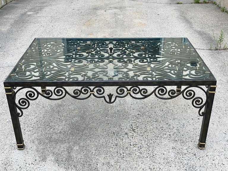 LaBarge scrolled cast iron cocktail table with brass accents in the form of an architectural gate or grille. Top inset with 3/8 inch thick flush-mounted glass. Black oxide finish. Labeled and numbered on underside.
 