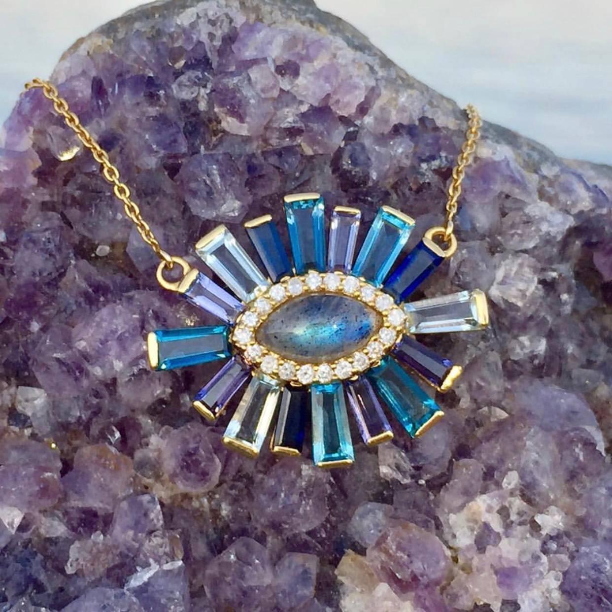 A marquise labradorite surrounded by a halo of diamonds radiated with a mix of aquamarine, iolite, sapphire, and tanzanite tapered baguettes.  Set in 18k yellow gold. 

Each piece of jewelry is handmade to order for you.  Production time is 4-6
