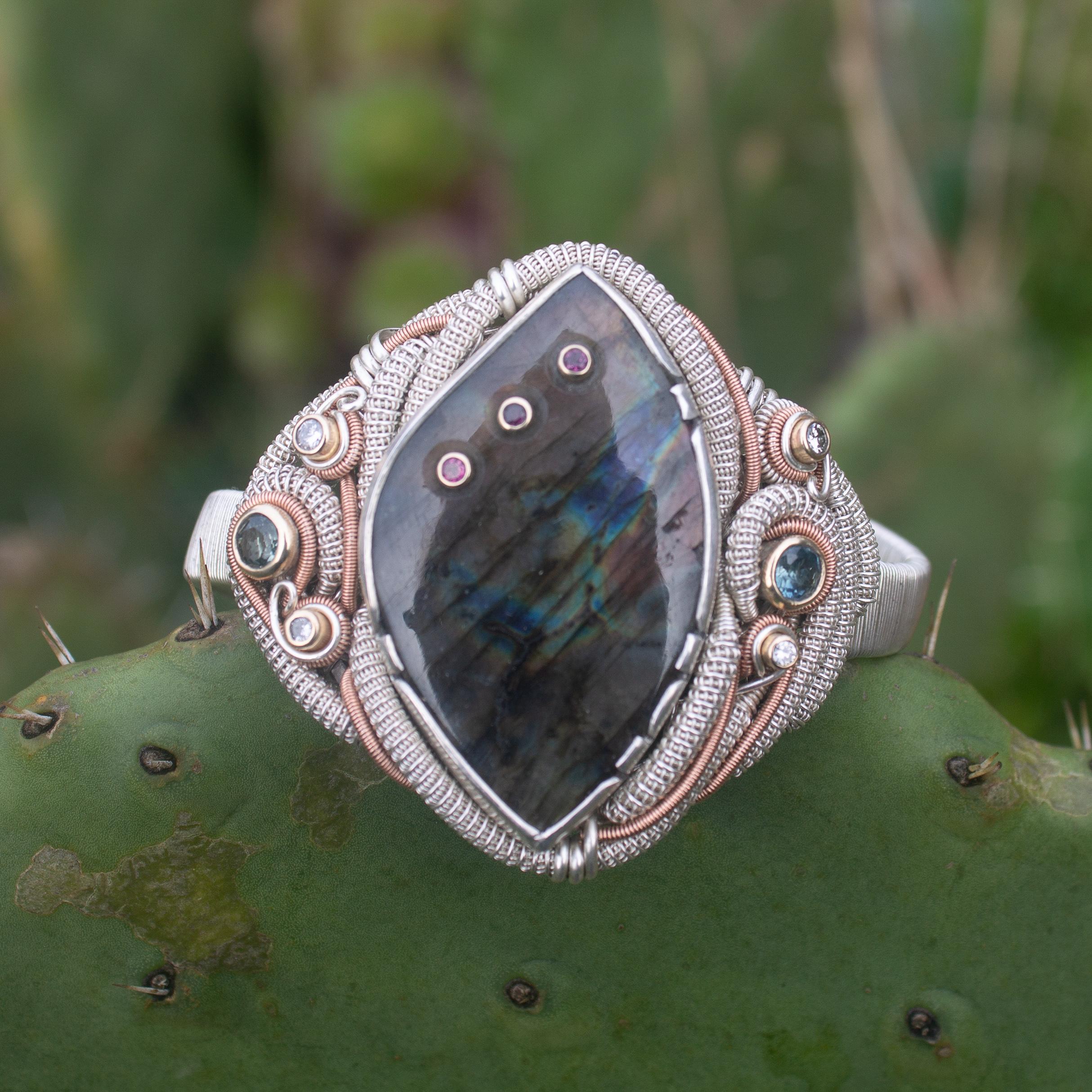 A gorgeous Labradorite with three purple Garnets set in the stone in 14 karat gold. Paired with Diamonds, Montana Sapphires, silver and 14 karat rose gold, this bracelet is truly one of a kind. Combining various techniques such as wire wrapping,