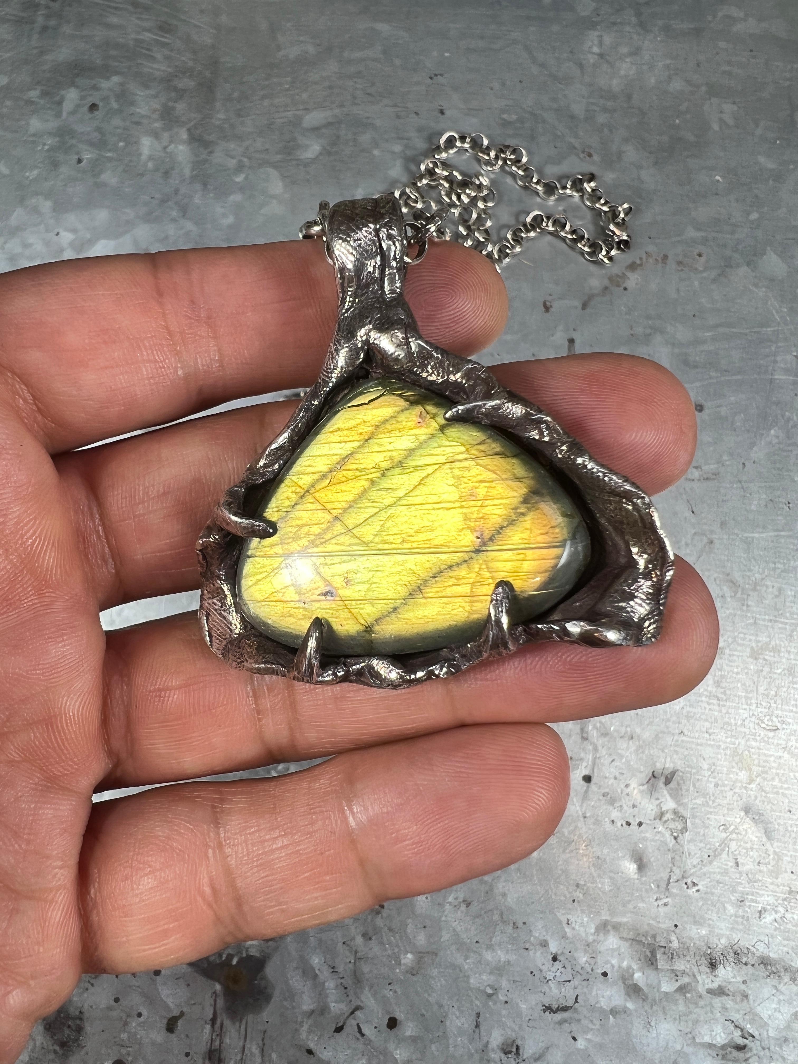 Ancient Light is a pendant created by Ken Fury featuring a rare and unique labradorite stone known for its iridescent play of colors. The stone's surface shimmers and changes color as the pendant is moved at different angles, reminiscent of a