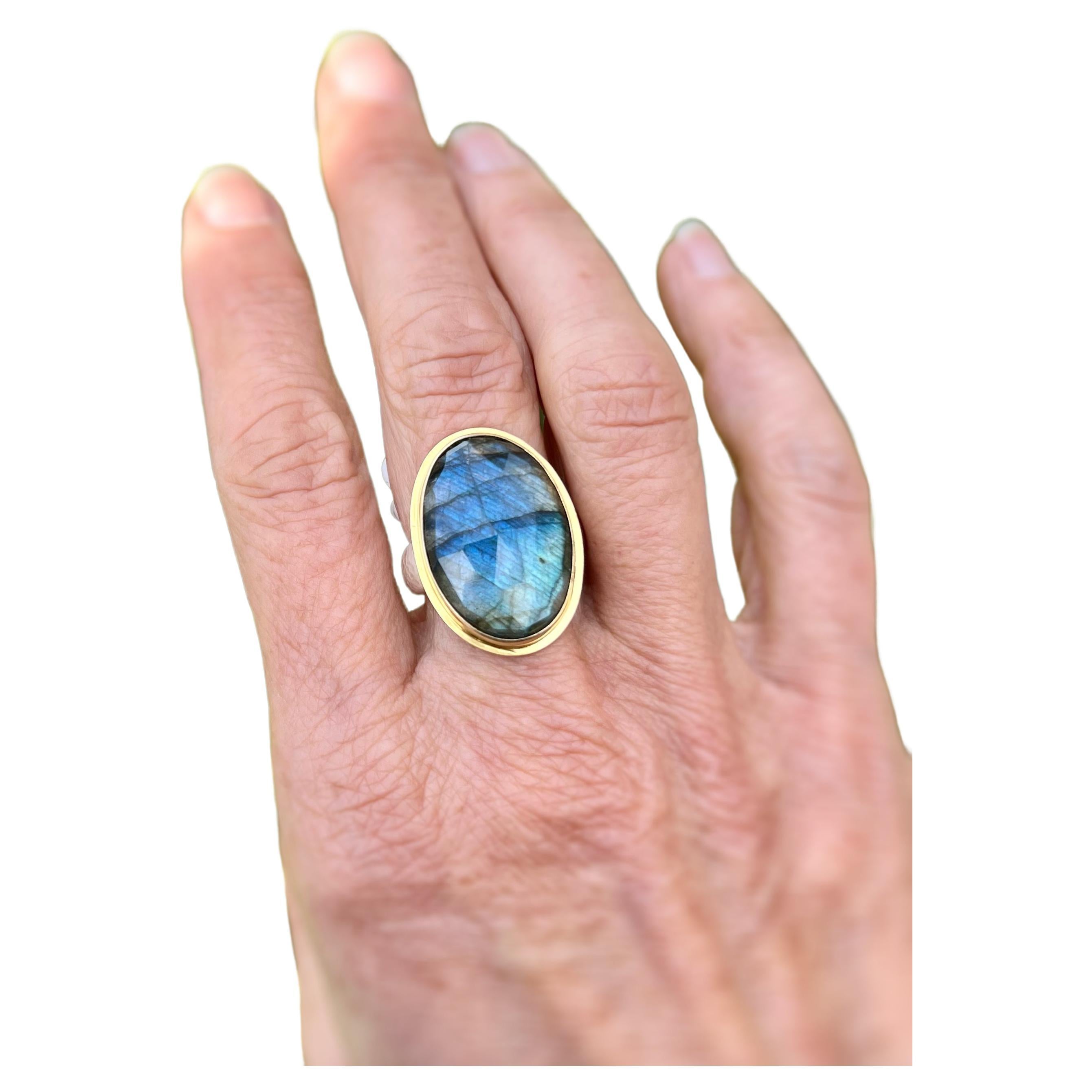 This Labradorite Oval is accented by a 18 karat gold step bezel and set in a hand hammered ring. Mesmerizing, this labradorite has a rainbow glow as one moves and sparkles with shades of peacock blue. The ring is a size 9 and can be sized to fit.