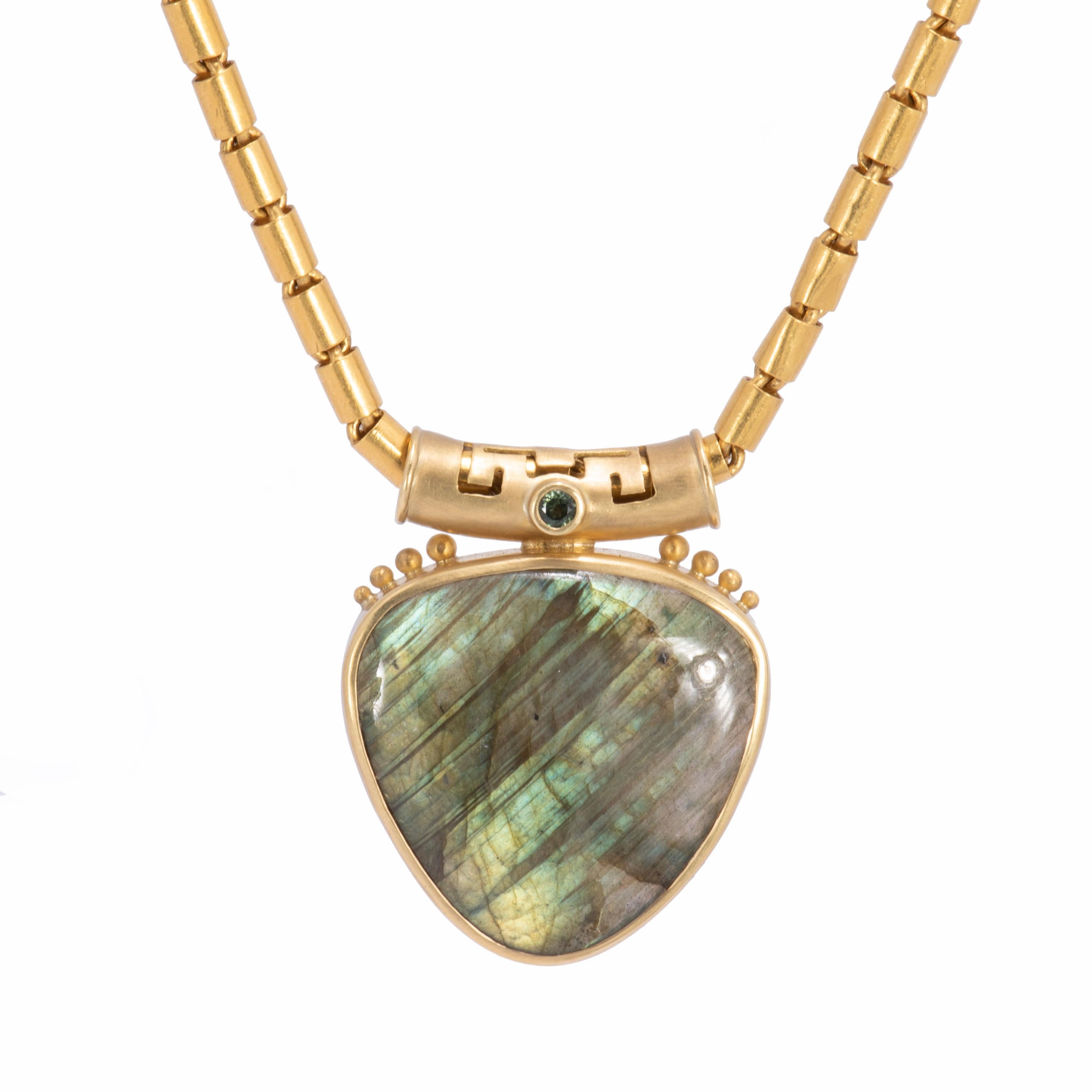 Our large green labradorite shield pendant is streaked with gold and pale blue lights and framed in 18 karat gold. Graduated gold beads along the crown highlight a curved slide bail like an Asian temple with geometric cutwork. A sparkling deep green