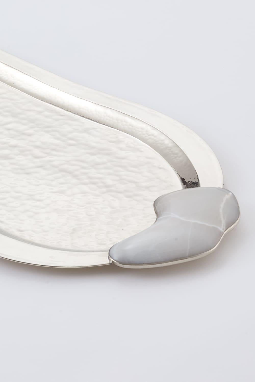 In the vast beauty of Argentine Patagonia, Lake Lácar inspires calm and elegance.
Its gentle shoreline takes shape in the curves of this tray: cool, luminous onyx reflecting the still waters, embraced by hand-hammered metal like the mountains that