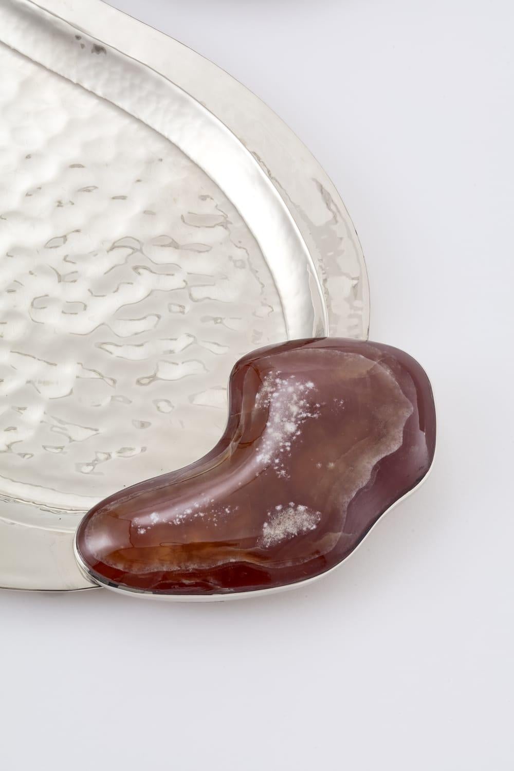 In the vast beauty of Argentine Patagonia, Lake Lácar inspires calm and elegance.
Its gentle shoreline takes shape in the curves of this tray: cool, luminous onyx reflecting the still waters, embraced by hand-hammered metal like the mountains that