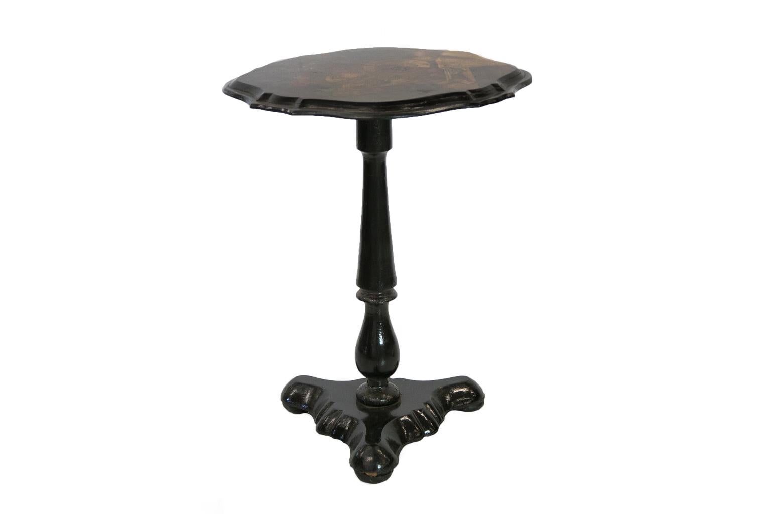 Lacquer and papier-mâché tilt-top table has a painting of still life depicting fruit and a jeweled urn. The top has a scalloped shape, and the turned stem terminates in a trefoil platform base.