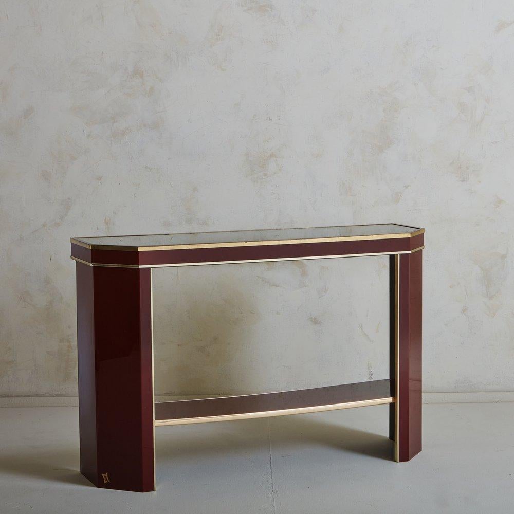 An elegant French console table in a deep burgundy hue with a lacquered finish. This piece has a patinated brass trim and an open lower shelf. Unknown manufacturers mark on the lower leg. Sourced in France, 1970s.

     
