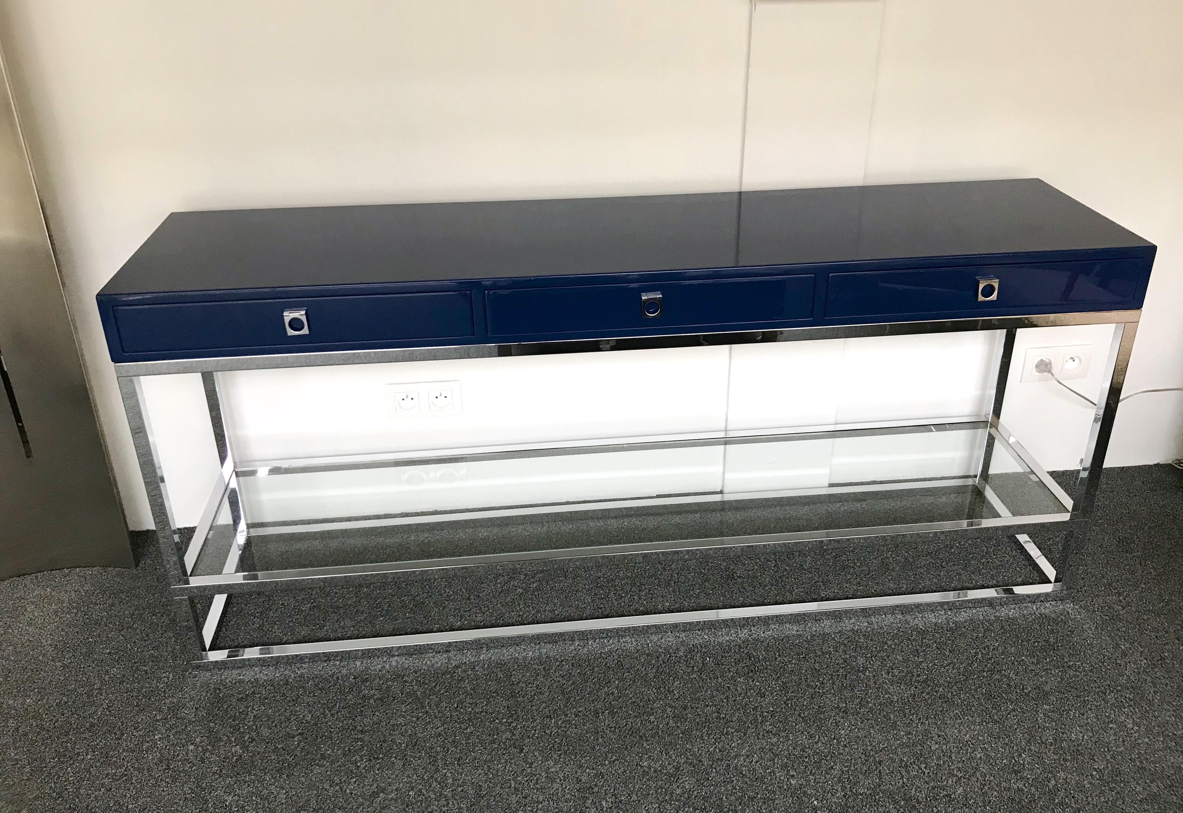 Rare long model of lacquered console table with 3 drawers in a blue lacquer, polished nickled brass feet and handle, low glass shelf by the designer Guy Lefevre for Maison Jansen. Special feet from the late 1970s in the Lefevre production, was