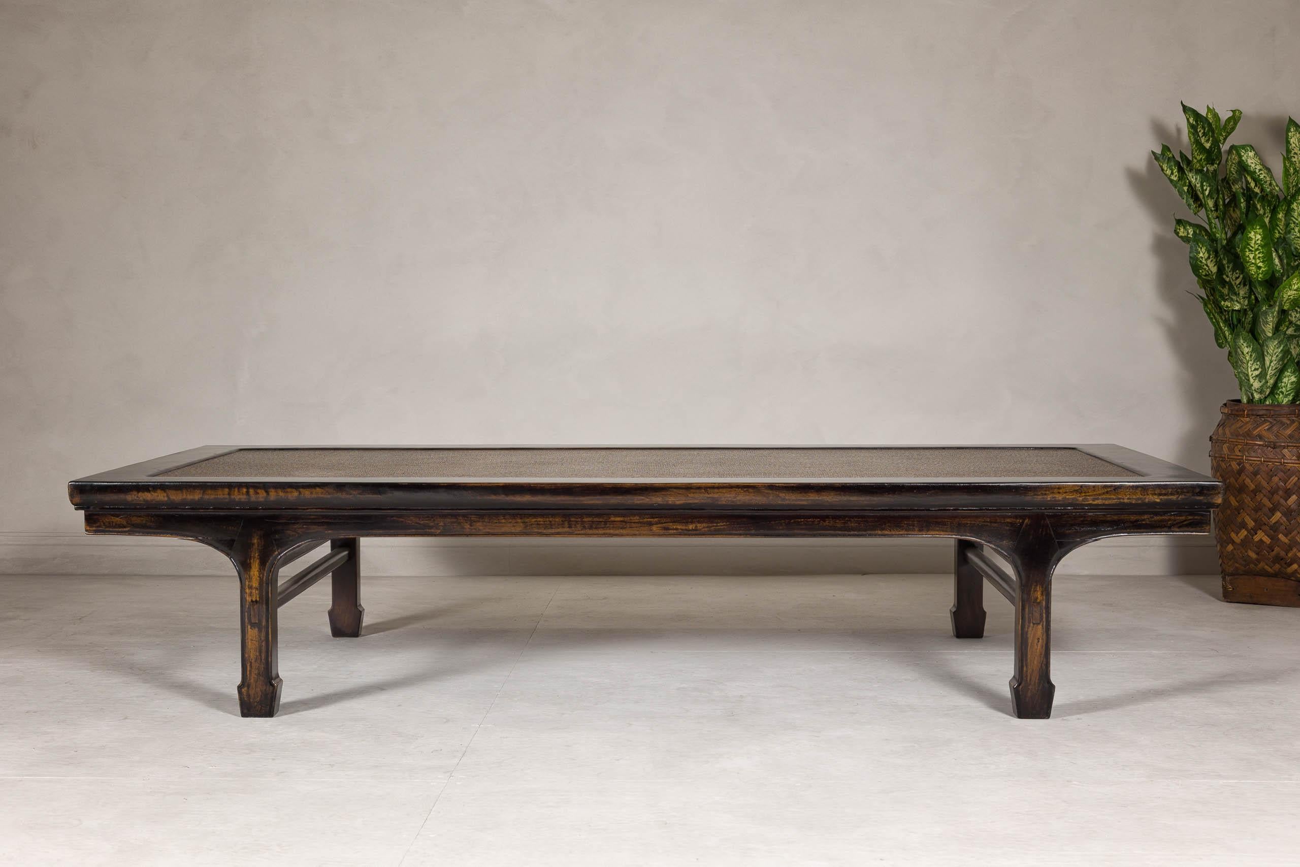 A Chinese Qing Dynasty period lacquered daybed or coffee table from the 19th century with woven matt rattan top and carved legs. Originating from the Qing Dynasty in the 19th century, this Chinese daybed or coffee table embodies the seamless blend