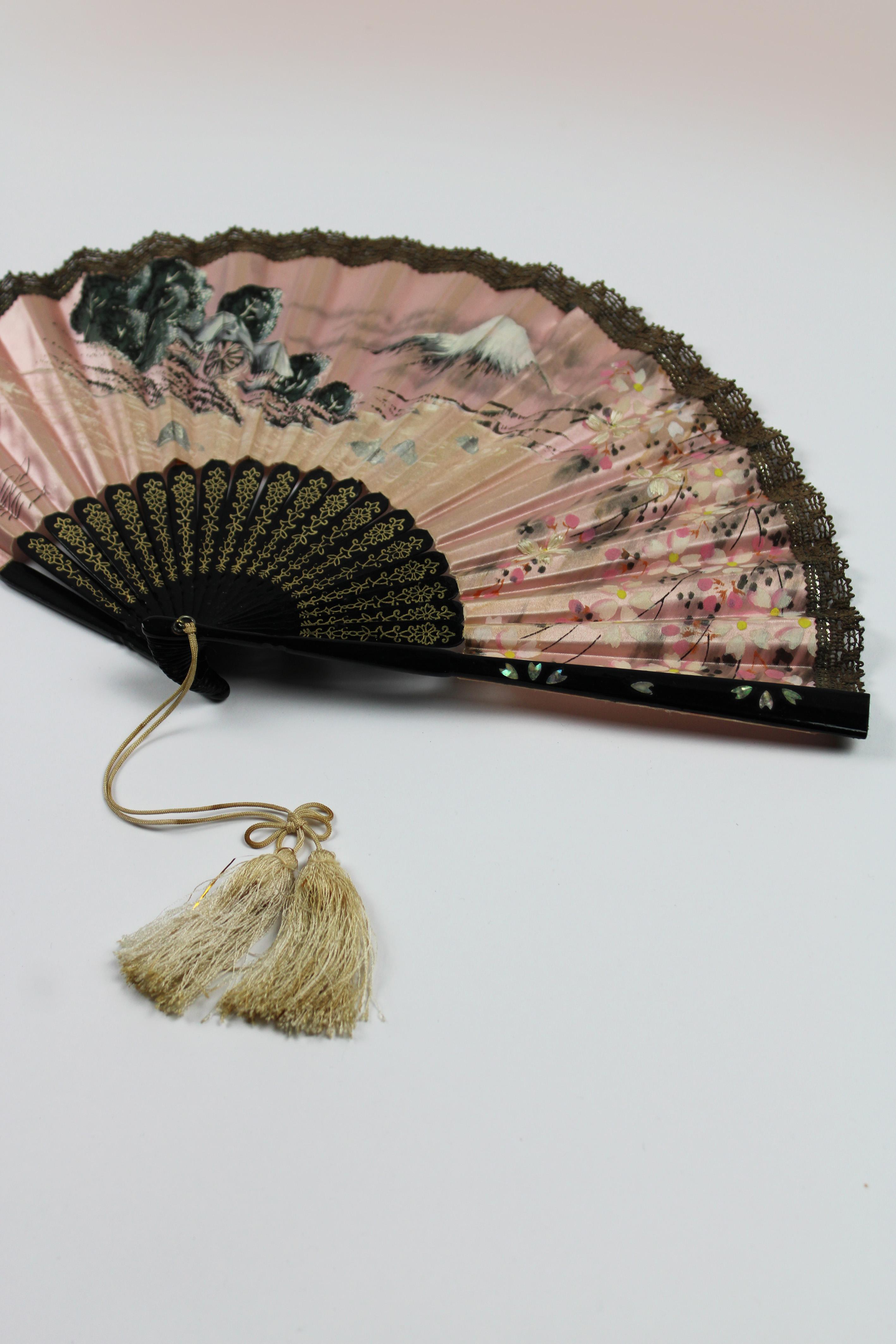 The lacquered handfan from Japan, dating around 1900, is a stunning example of traditional craftsmanship and artistry. The fan's structure is coated with a rich black lacquer finish, providing subtle inlays of mother of pearl are carefully embedded