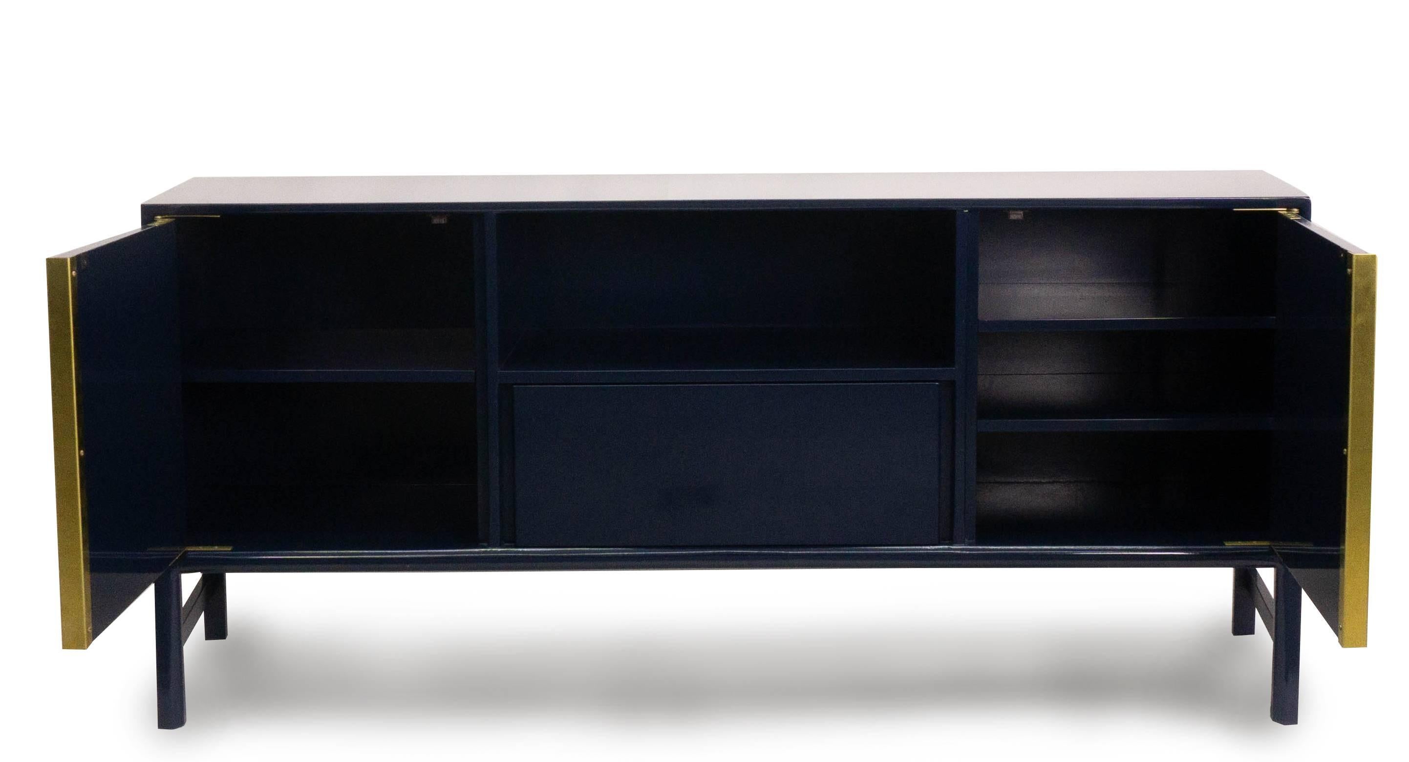 Our boomerang sideboard is lacquered in high gloss Benjamin Moore Dark Royal Blue. This modern console features cabinets, a centre drawer and a shelf. The cabinet doors are finished with a decorative treatment that provide depth and texture and are