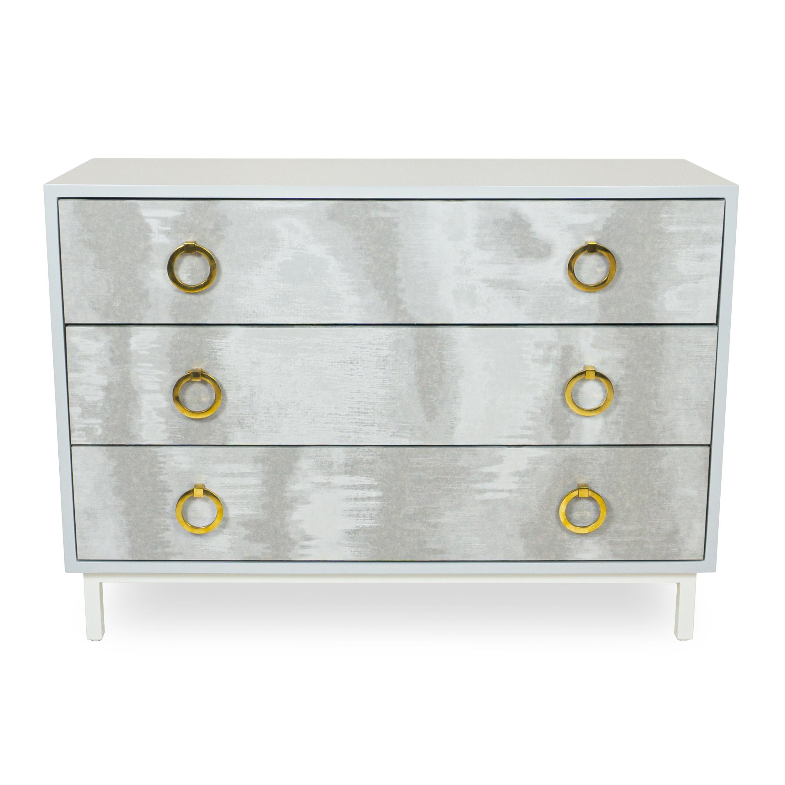Chest of three drawers (dresser, bedside, hall table) lacquered light blue. Drawer faces finished with subtly shiny moire material and with round gold pulls. Slow close hardware. Base lacquered white.

Measurements:
Overall: 42”W x 15.5”D x