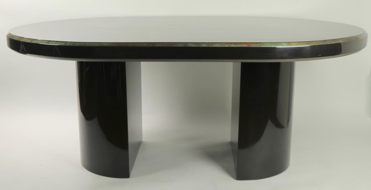 Chic oval dining table having a black lacquered top, with a silvered beveled edge, and two opposing semi circular pedestal legs. Very well designed and constructed, the top surface does show three parallel cracks which run the width of the top (see