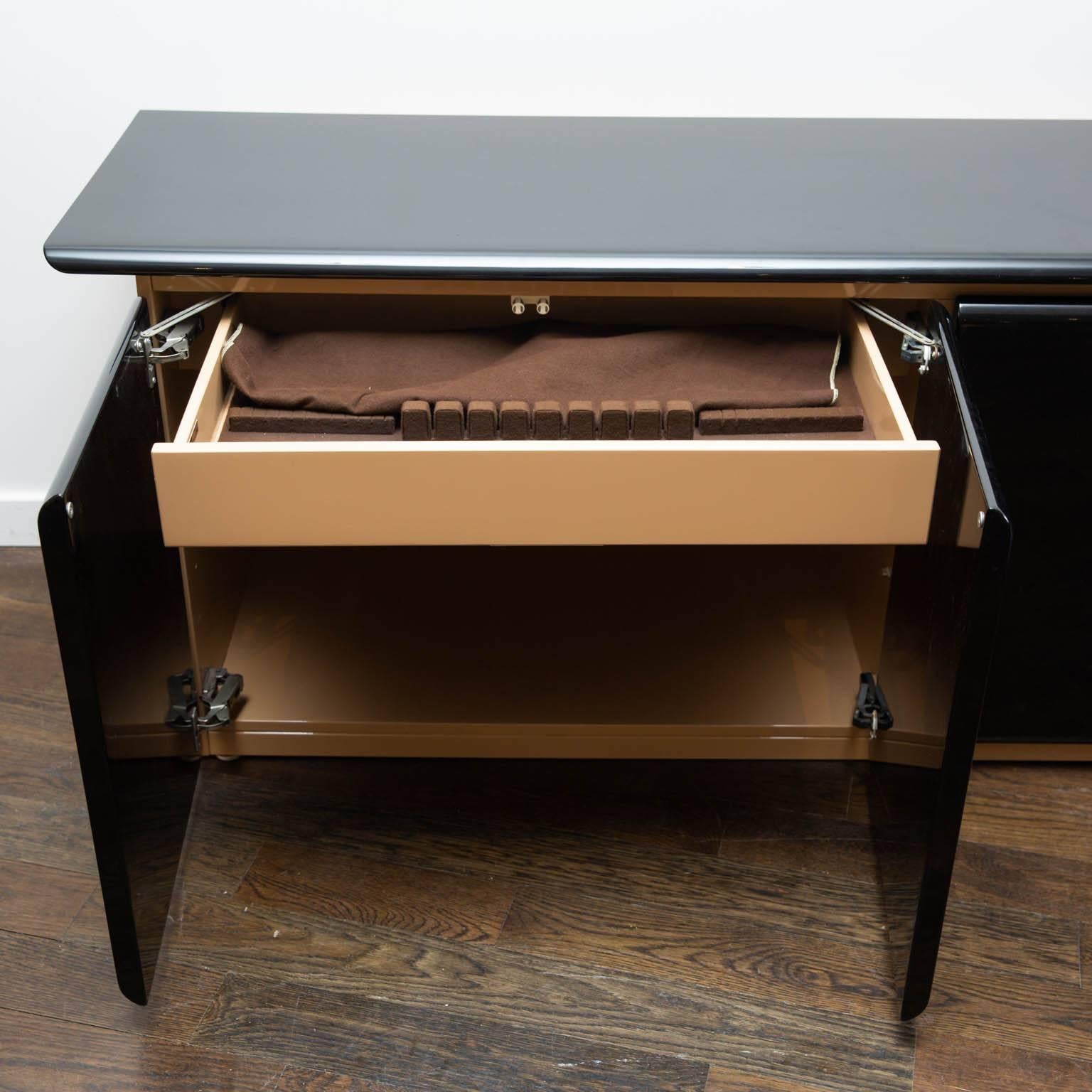 Modern sideboard in a two-toned beige and black lacquer. With silverware drawers and two interior shelves. Interior lights up on right side.