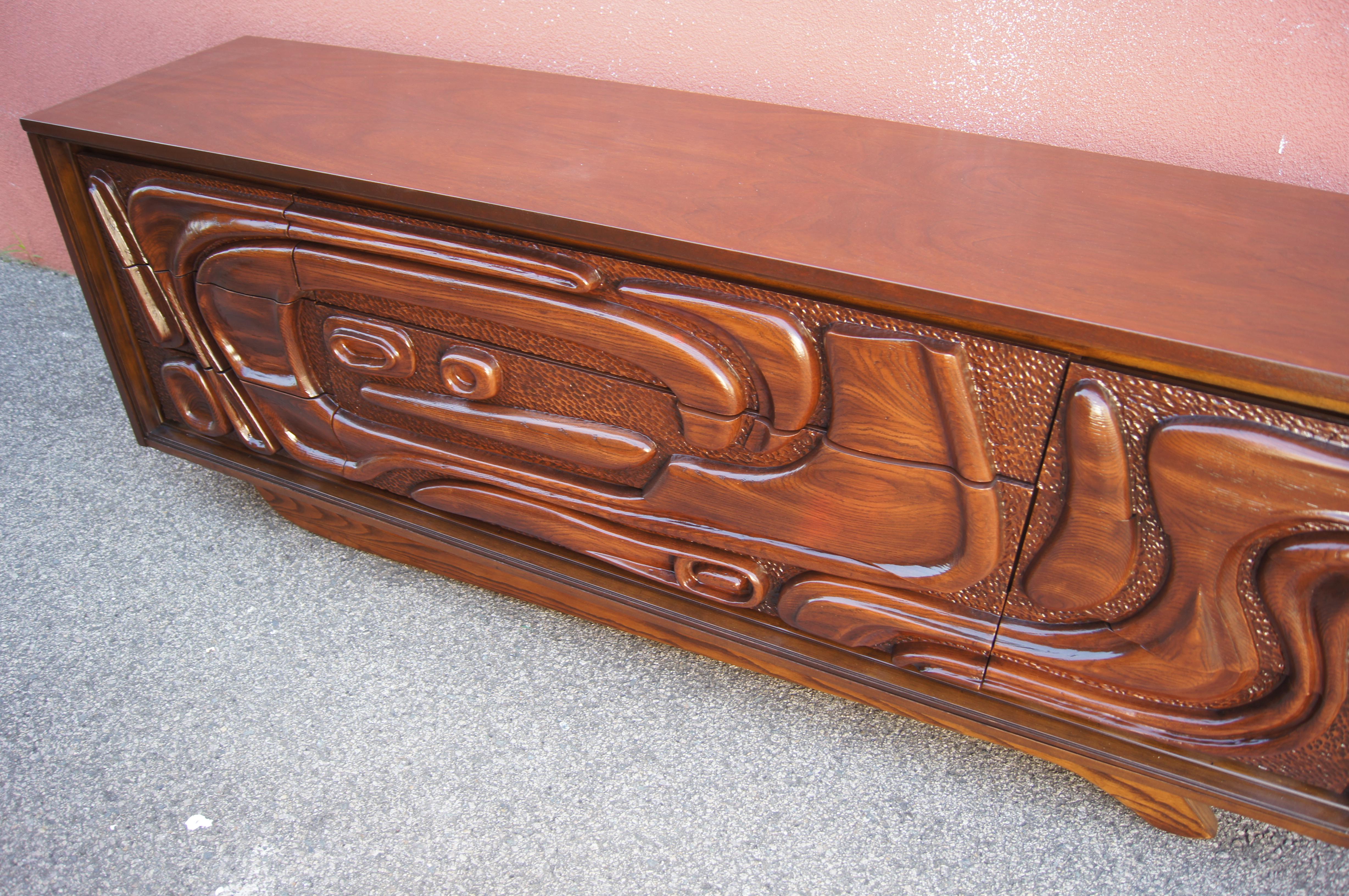 This lacquered walnut dresser comes from the oceanic series produced by Pulaski Furniture in the late 1960s and appearing, notably, in the television series Mad Men. An exuberant sculptural front, with formica bas reliefs referencing Pacific Island