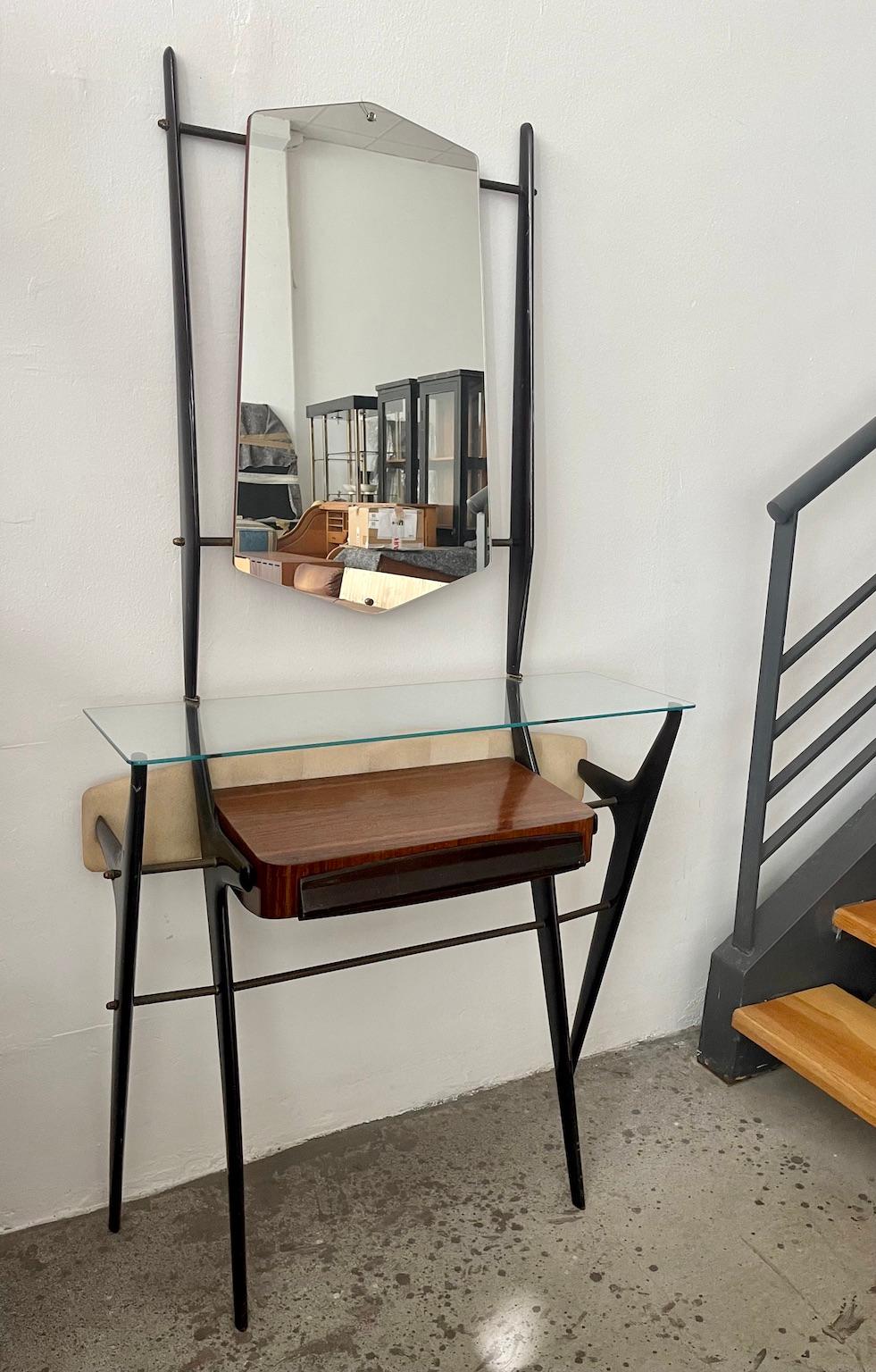 Console / vanity table with a glass top, wooden drawer compartment and a mirror. Scissor-legged structure made of lacquered hardwood with brass clips. Back platform upholstered in leatherette with screws to attach the piece to the wall if desired.