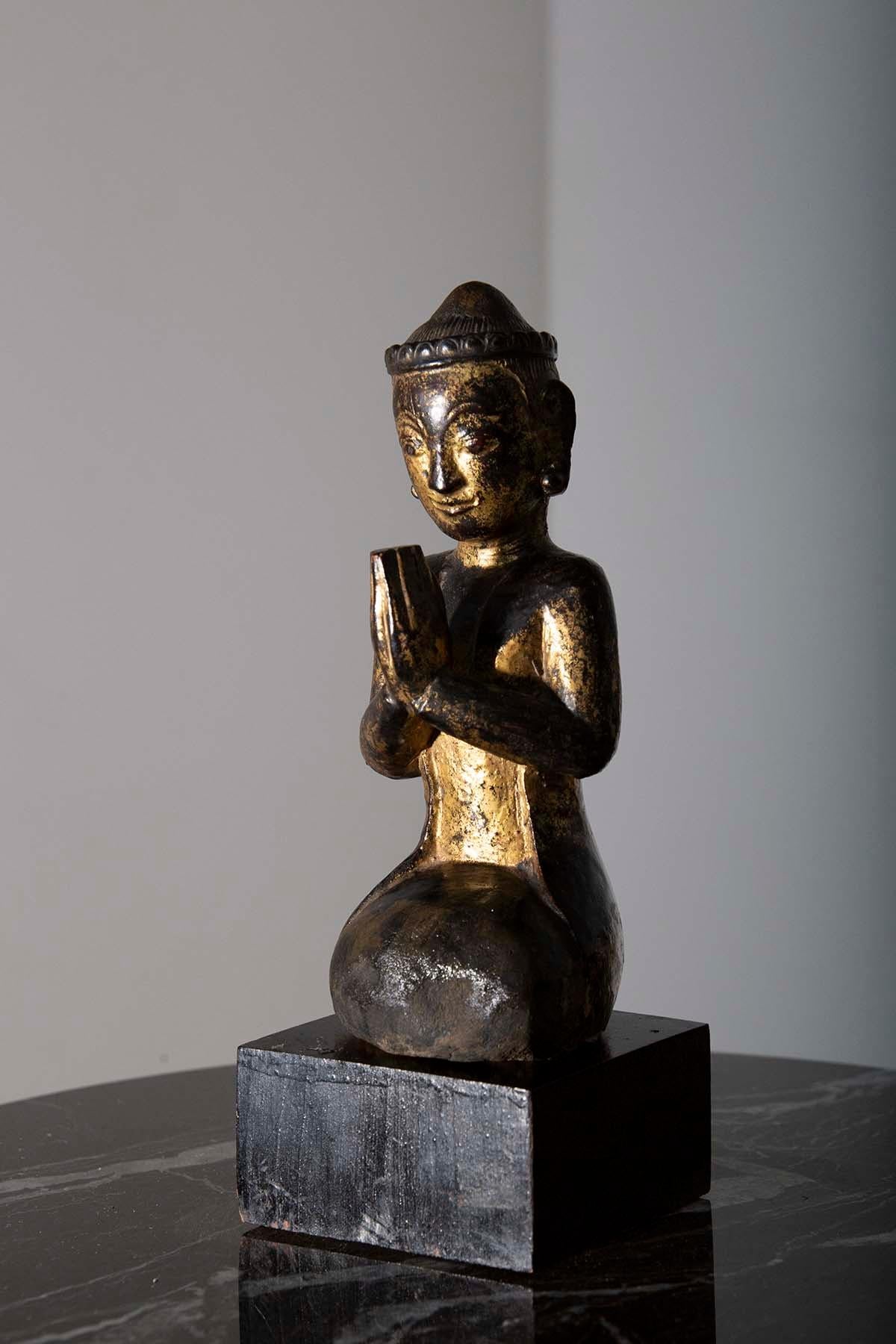 In the early 19th century, in the heart of Burma, a small but profoundly meaningful masterpiece emerged—a lacquered wooden sculpture that captures the essence of devotion and prayer. This exquisite creation, depicting a praying monk or orant, is a