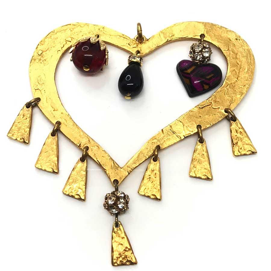 The pendant is from the House of CHRISTIAN LACROIX. In metal gilded with fine gold, it represents the outline of a heart to which pendants are attached. It leaves a heart hanging on which we perceive a purple swallow, and two other teardrop charms,
