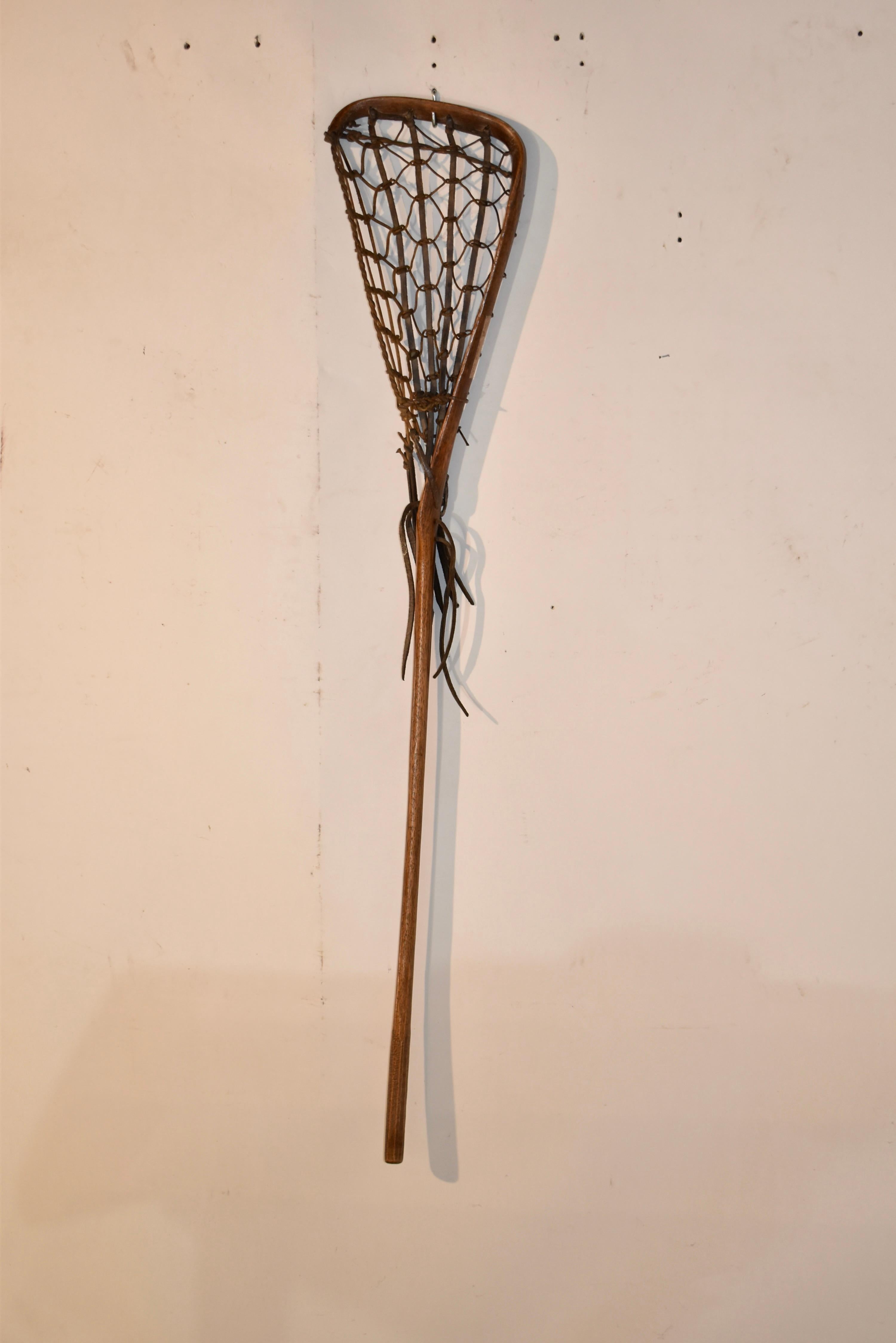 Palo de lacrosse de la década de 1920 fabricado en nogal americano. La red está tejida con cuero y cordel. Se trata de un palo de madera curvada con una bonita forma que quedaría genial en cualquier habitación de la casa.