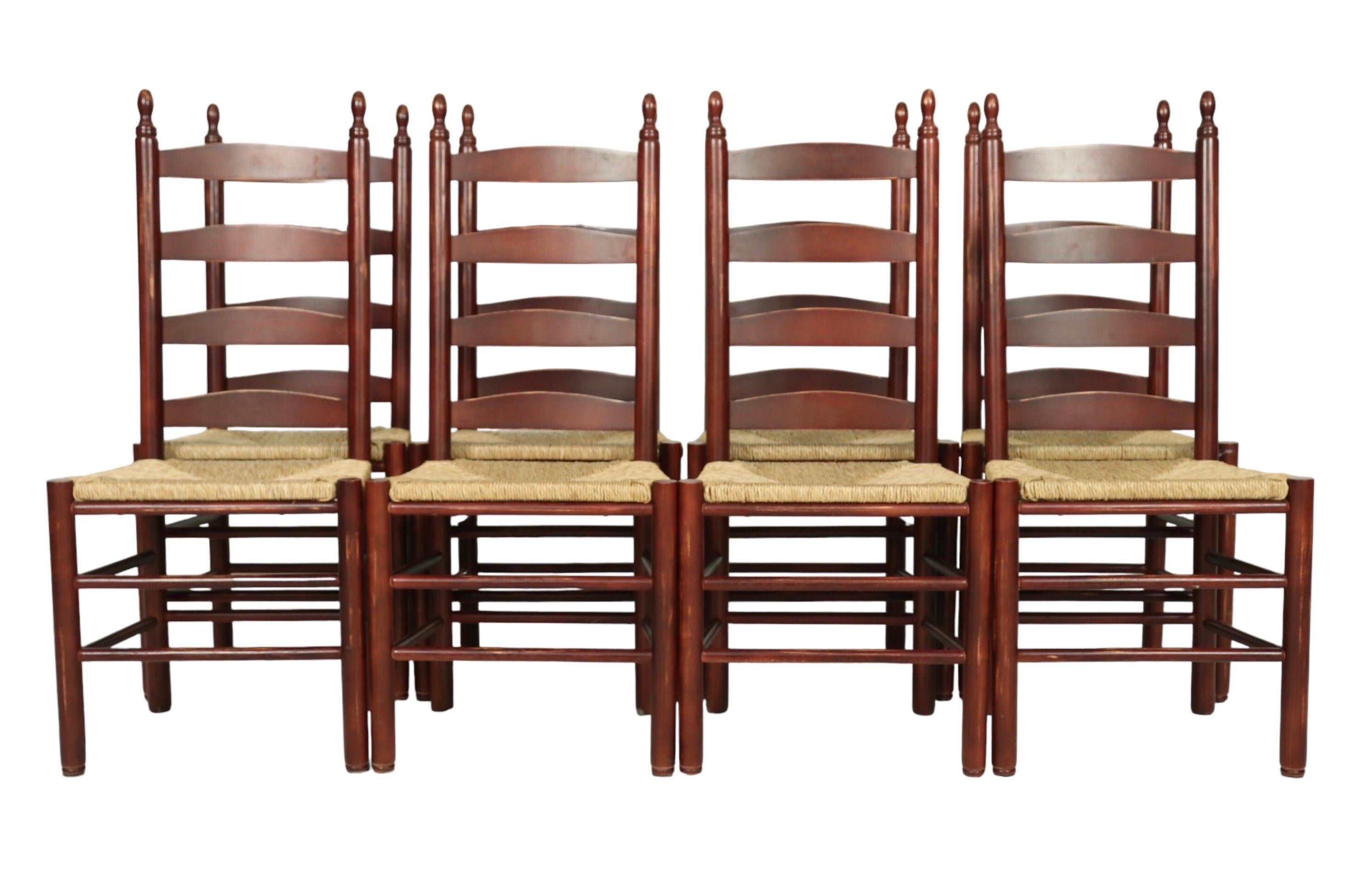 A set of eight Shaker style dining side chairs made of oak and stained red. Turned finials top posts to each side of ladder backs above square woven rush seats. Round turned legs are supported with two box stretchers. Dimensions per chair.