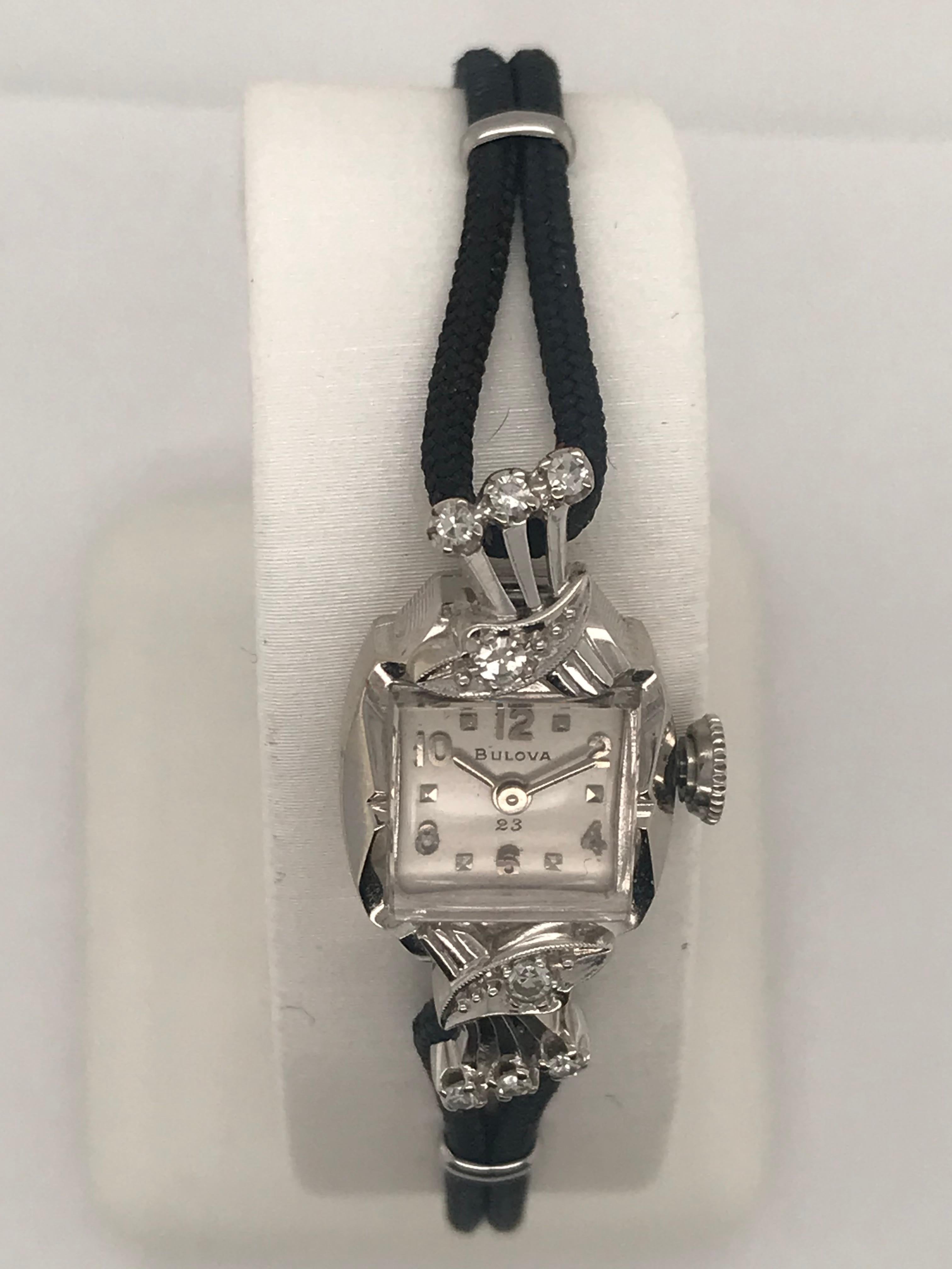 This Dainty 14K white gold vintage Bulova is a 17 jewel manual wind watch.  It is circa 1958 with eight single cut diamonds that weighs .16cts total weight.  It also has a black double cord strap secured with a white safety chain that is attached by