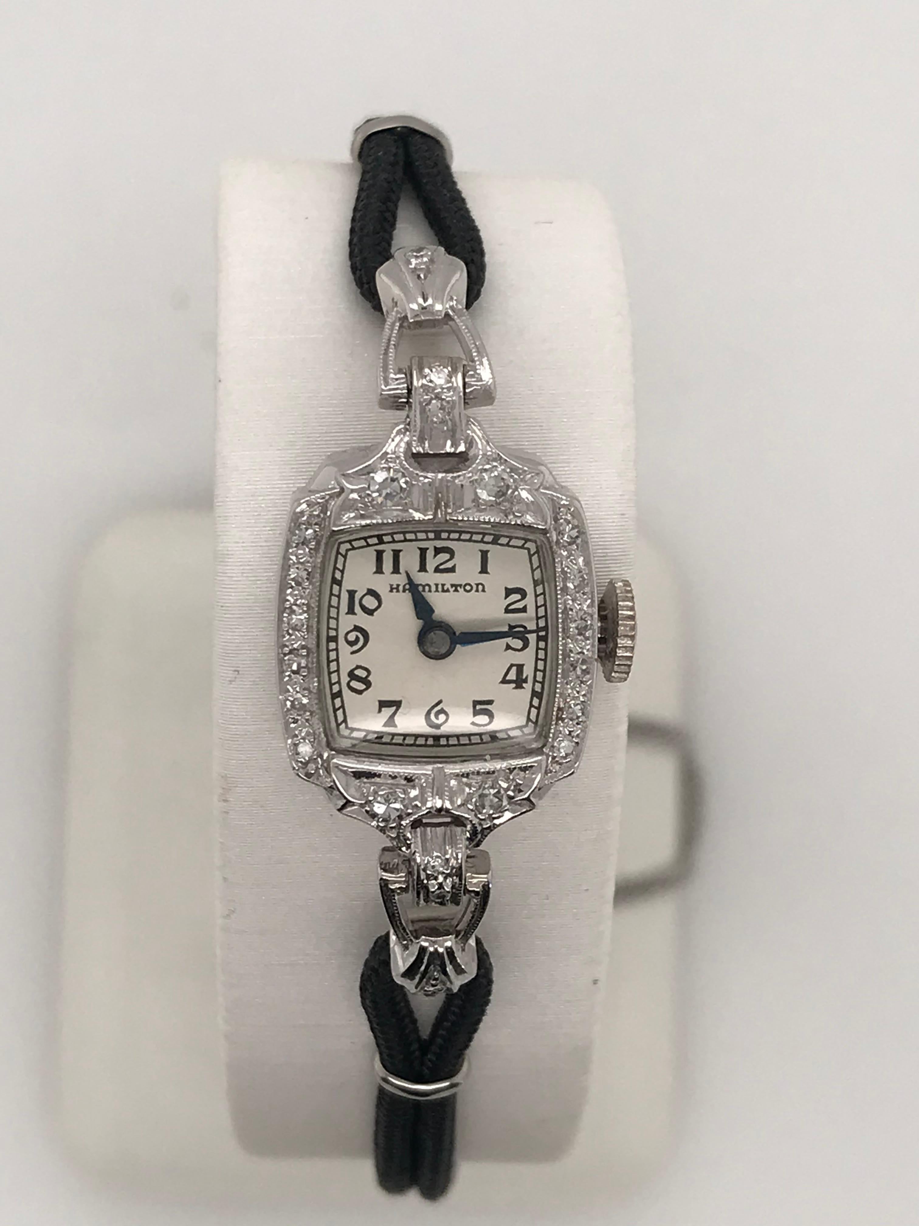 14K white gold lady's Hamilton watch 17 jewel manual wind watch with black cord strap and 20 single cut diamonds=.20cts total weight.  This watch also has a white chain connected to the fold-over clasp.  This petite timepiece will add a touch of