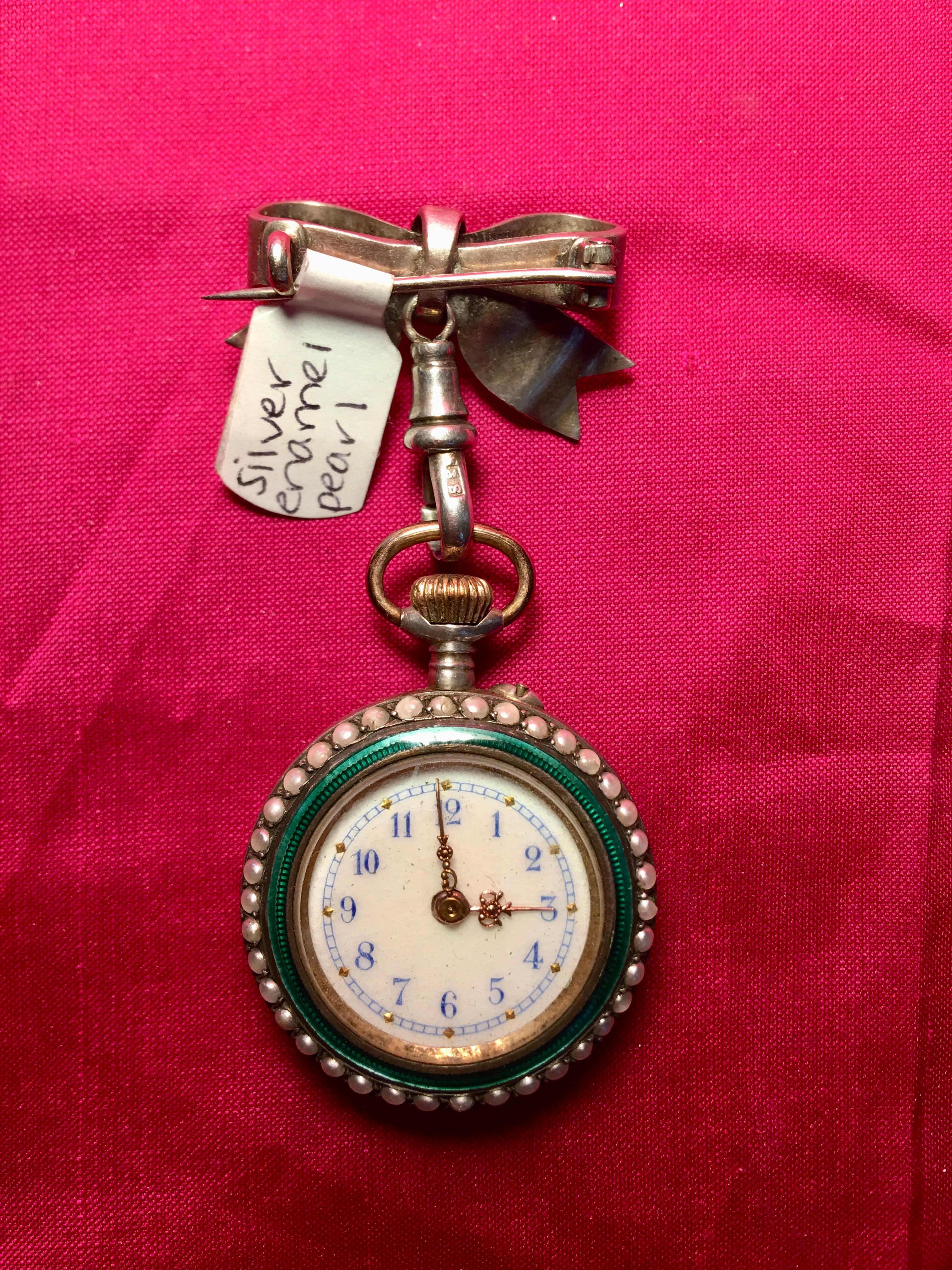 A beautifully handcrafted emerald ladies fob watch. The watch has a lovely enamel dial with Arabic numerals. There are pearls surrounding its outer silver case. It is hand wound with a pin set. At the back of the watch is a wonderful picture of a