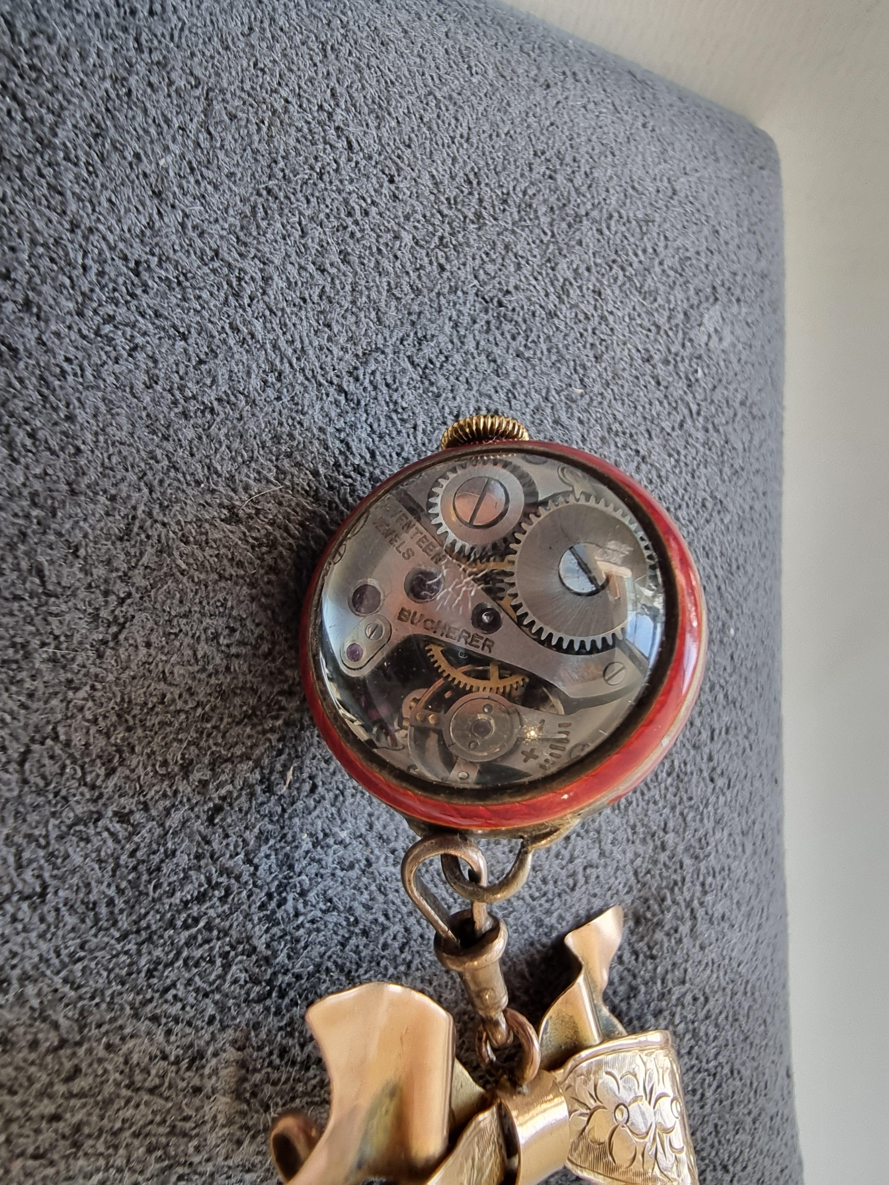Unusual gold and red guilloche enamel brooch watch by Bucherer. Held by an engraved bow the watch fully signed Bucherer, 17 jewels, Swiss, is viewed through a bubble glass. Turning the watch over the movement is revealed through another bubble glass