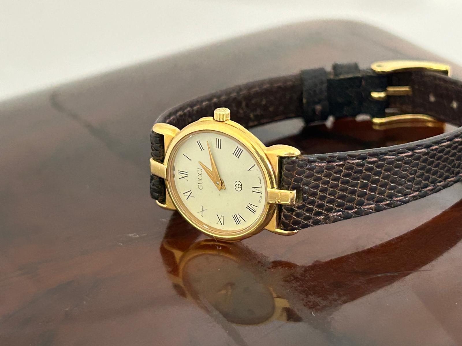 Notre référence Gucci 3400L / 3400FL pour dames est dotée d'un boîtier en acier inoxydable plaqué or de 24 mm (couronne incluse) et d'un bracelet en cuir Gucci d'origine avec boucle Gucci en ton or. Présentée en excellent état, sans dégradation