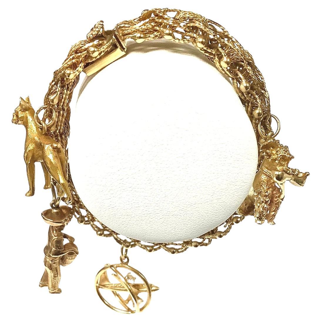 Ce bracelet à breloques en or 14 carats des années 1960 est orné de quatre (4) breloques uniques. Le bracelet en or à double maillon, d'une longueur de 7 pouces, est doté d'un fermoir à pression avec crochet de sécurité et d'une chaîne de soutien