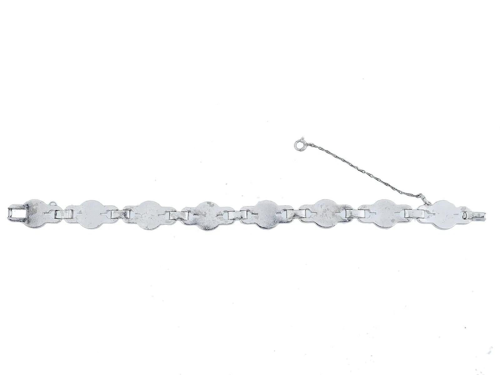 A ladies silver bracelet features a symmetrical design with repeating links, each consisting of a central round light blue stone surrounded by small clear stones. A safety chain is attached near the clasp. Marked with initials E. B. on the clasp.