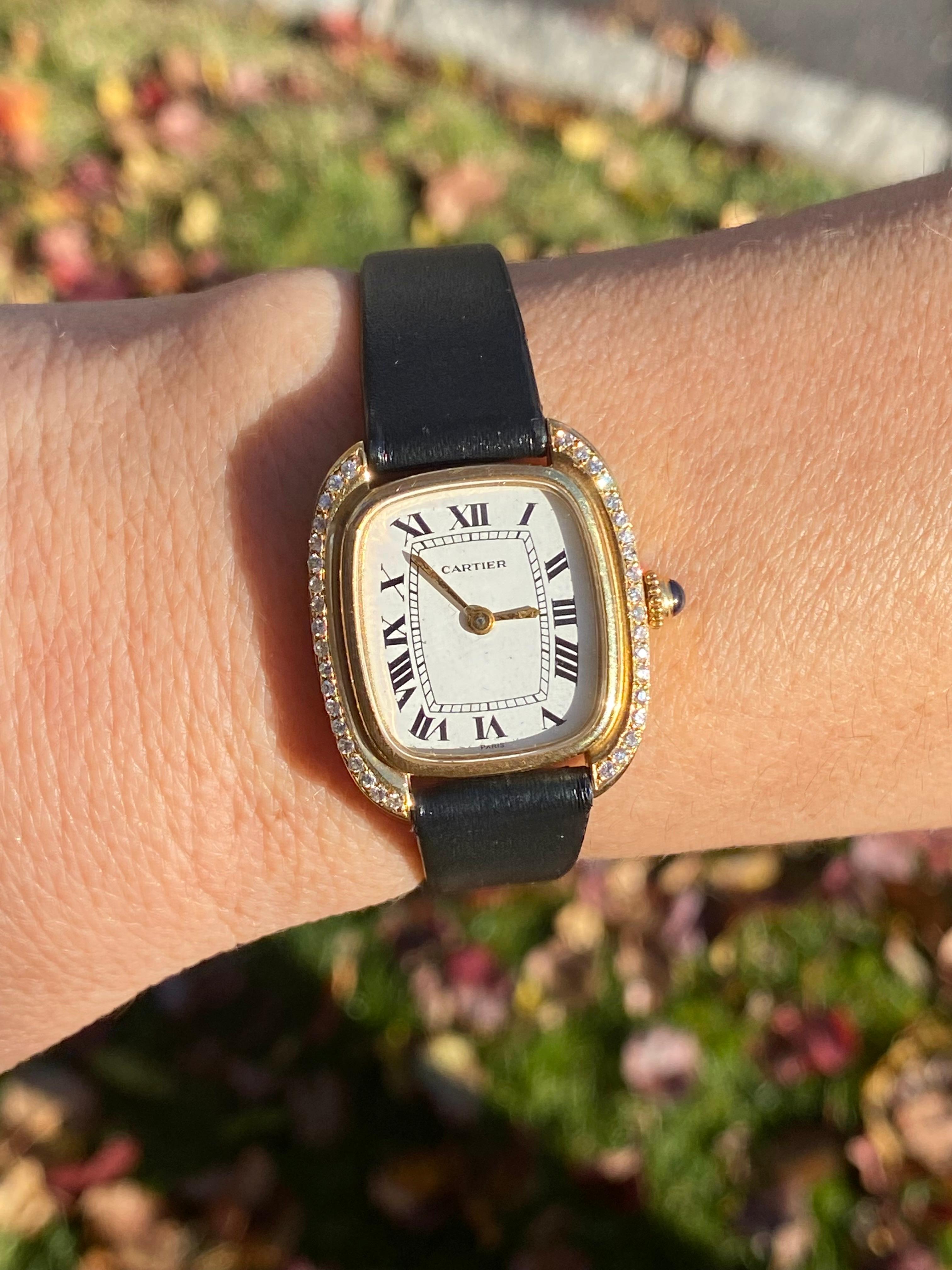 The oval-shaped case is decorated by a single outer row of round full cut diamonds, a white dial with black Roman numerals, gold hands, manual movement, genuine leather replacement strap, and complete with a cabochon cut sapphire crown. The back