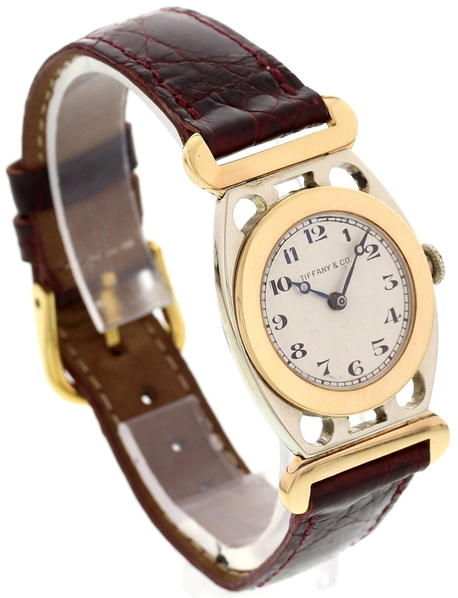 Ladies Tiffany & Co vintage watch. 26 mm 18k white gold case. 18k yellow gold fixed bezel. 18k yellow gold lugs. White dial with blue hands and black Arabic numerals. Adjustable red leather strap with gold tone stainless steel buckle. Mechanical