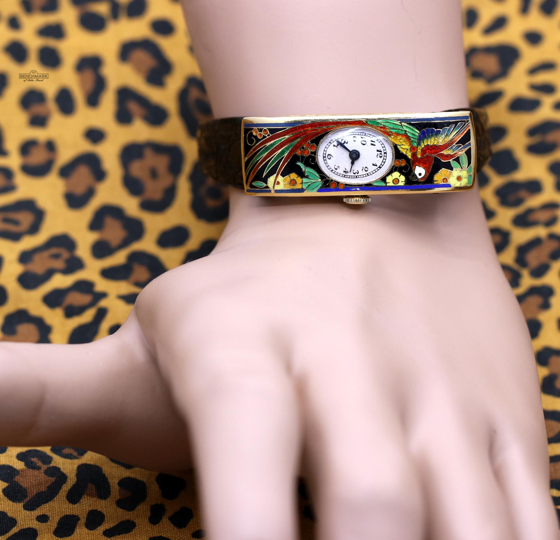 An 18K yellow gold watch, with a case measuring 40mm X 14mm, and featuring a beautifully enameled parrot with flowers, in bright, vivid colors. This watch also features a black crocograin strap.