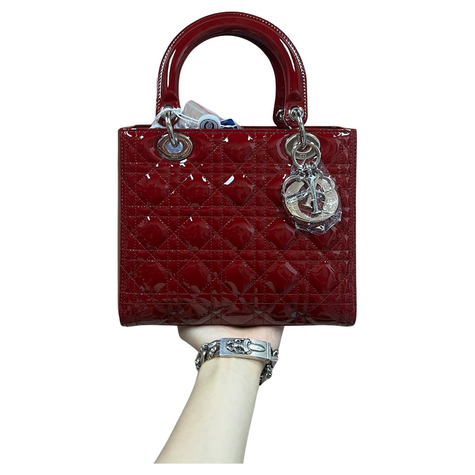 The Lady Dior bag is an epitome of elegance and beauty. Accentuate your look with the timeless style of Medium Lady Dior, crafted in Burgndy Patent Leather. This classic bag features a cannage stitch, creating a beautiful silhouette and an instantly