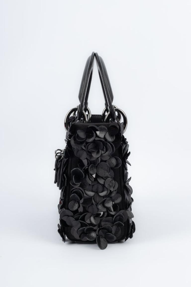 Dior - (Made in Italy) Black leather and satin bag ornamented with leather and sequins flowers. Silvery metal elements.

Additional information:
Condition: Very good condition
Dimensions: Length: 17 cm - Height: 15 cm - Depth: 5 cm - Handle: 25 cm