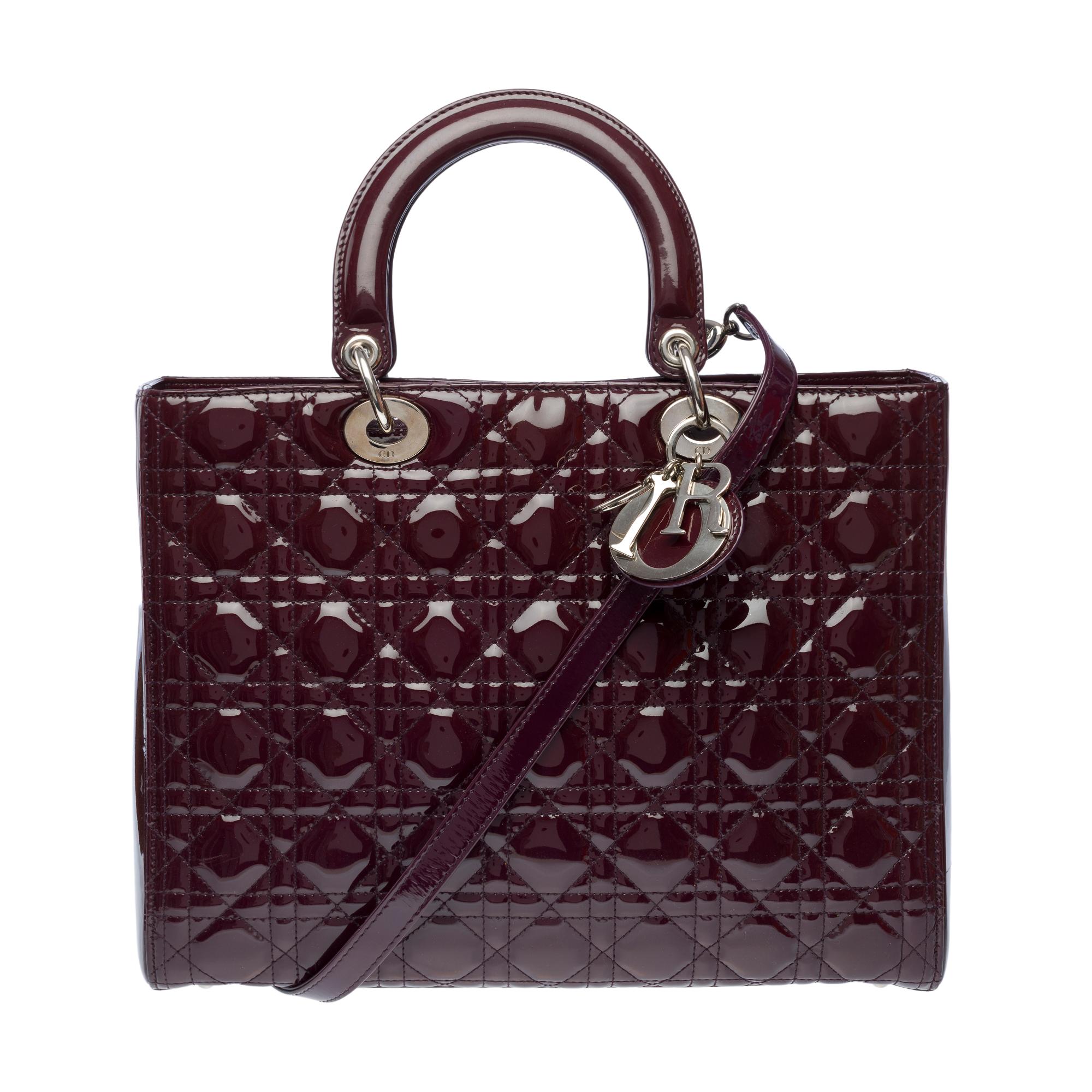 Superb​ ​Lady​ ​Dior​ ​handbag​ ​large​ ​model​ ​(GM)​ ​in​ ​Purple​ ​patent​ ​leather,​ ​silver​ ​metal​ ​trim,​ ​double​ ​burgundy​ ​leather​ ​handle​ ​and​ ​a​ ​removable​ ​strap,​ ​allowing​ ​hand​ ​and​ ​cross​ ​body​ ​carry

A​ ​zipped​