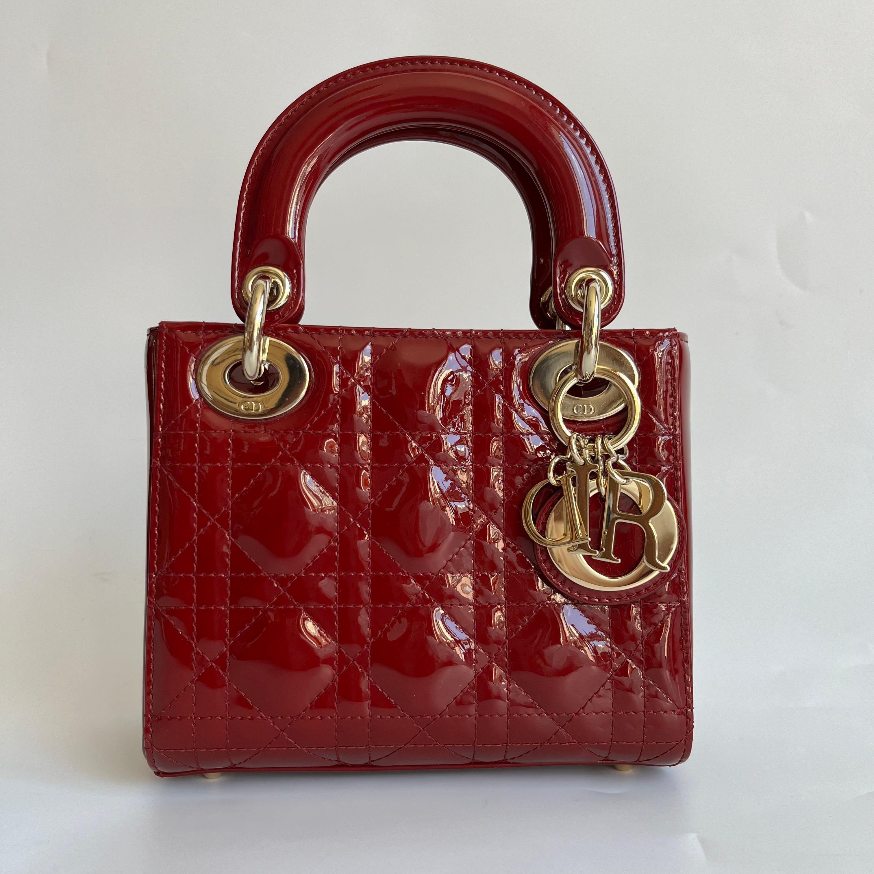 Questa borsa Lady Dior Mini è caratterizzata da uno splendido colore rosso in pelle verniciata decorata con hardware dorato e tracolla a catena impreziosita d'oro, che la rende un accessorio ideale per ogni donna elegante che osa fare una