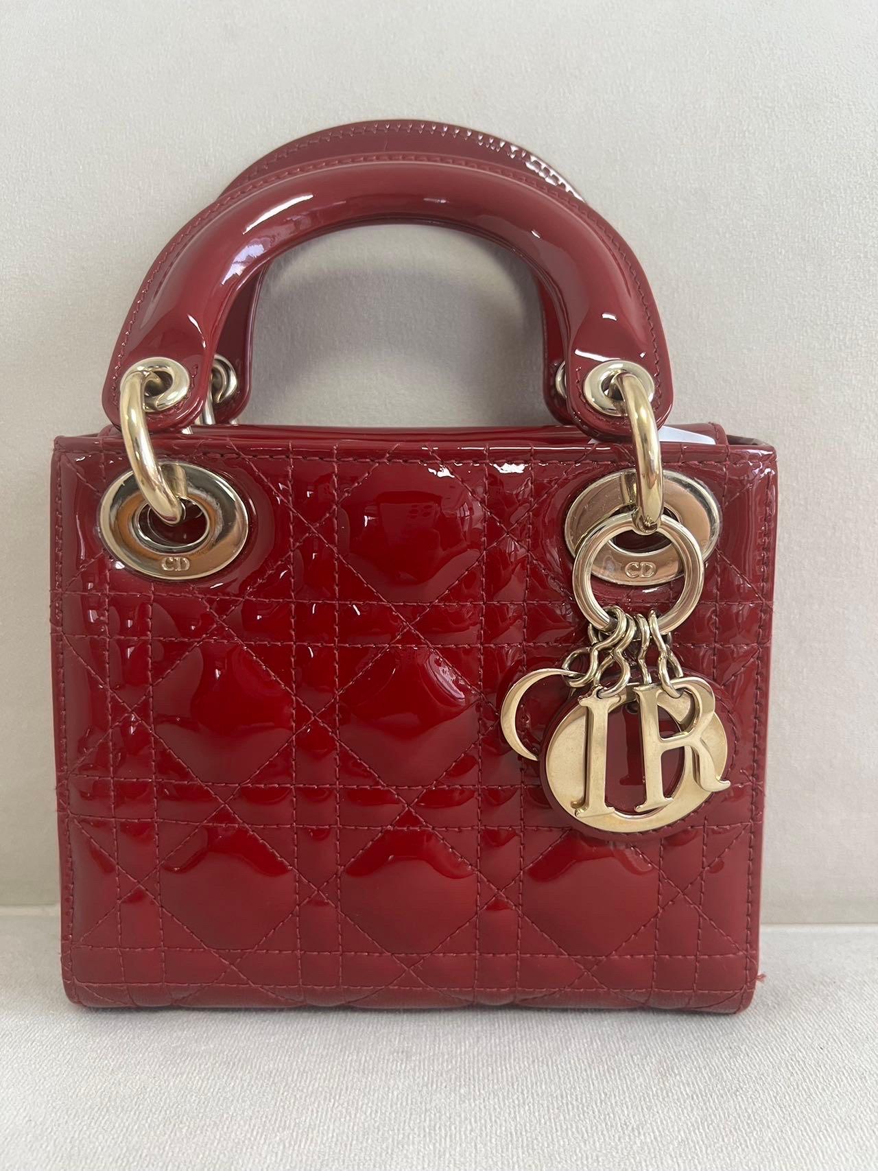 Questa borsa Lady Dior Mini è caratterizzata da uno splendido colore rosso in pelle verniciata decorata con hardware dorato e tracolla a catena impreziosita d'oro, che la rende un accessorio ideale per ogni donna elegante che osa fare una