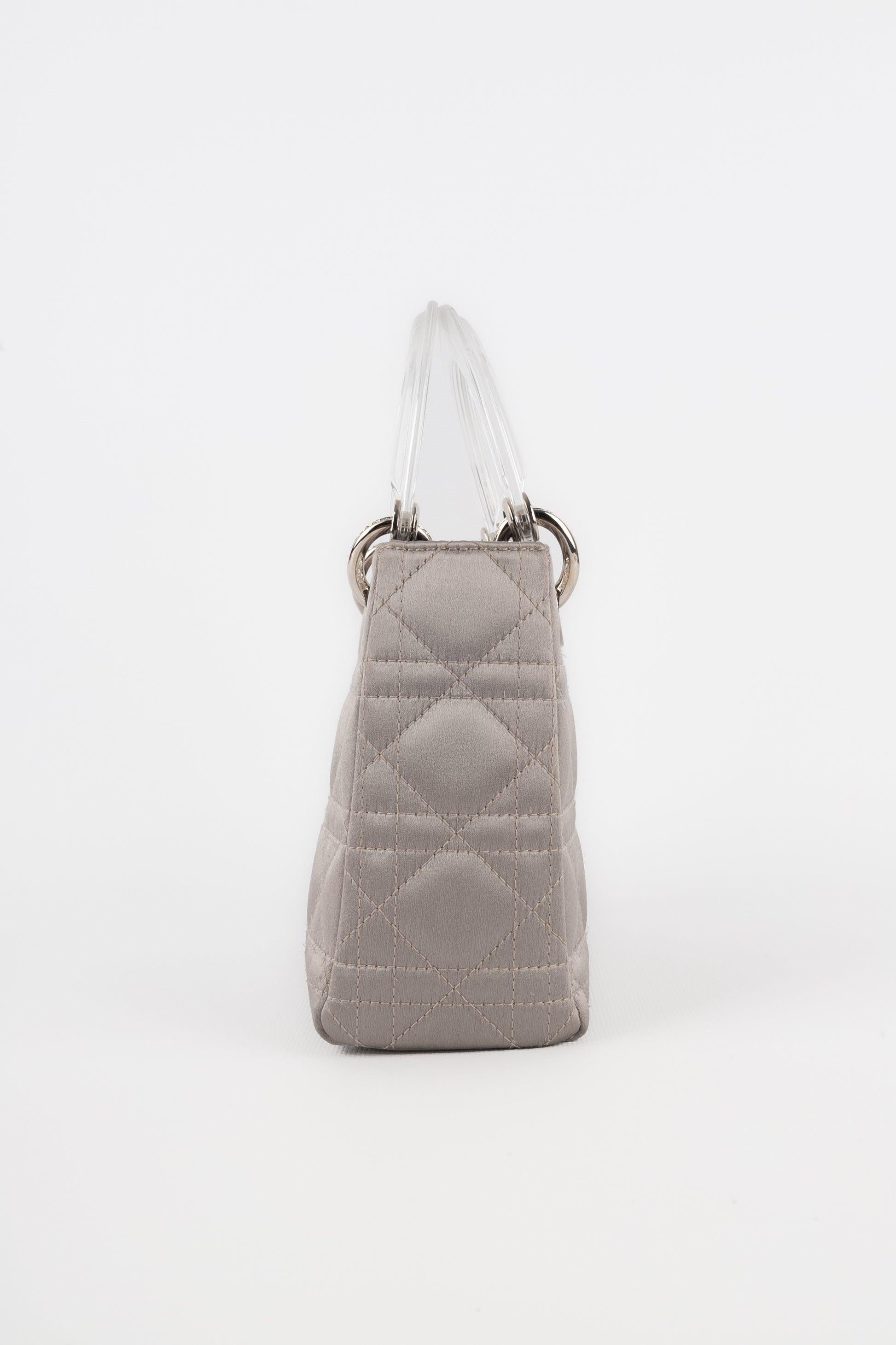 Dior - (Fabriqué en Italie) Mini sac 'Lady Dior' en satin gris perle avec des surpiqûres de canevas. Éléments et charms en métal argenté rehaussés de strass. Double poignée en bakélite translucide, dont l'une contient des charmes alphabétiques pour