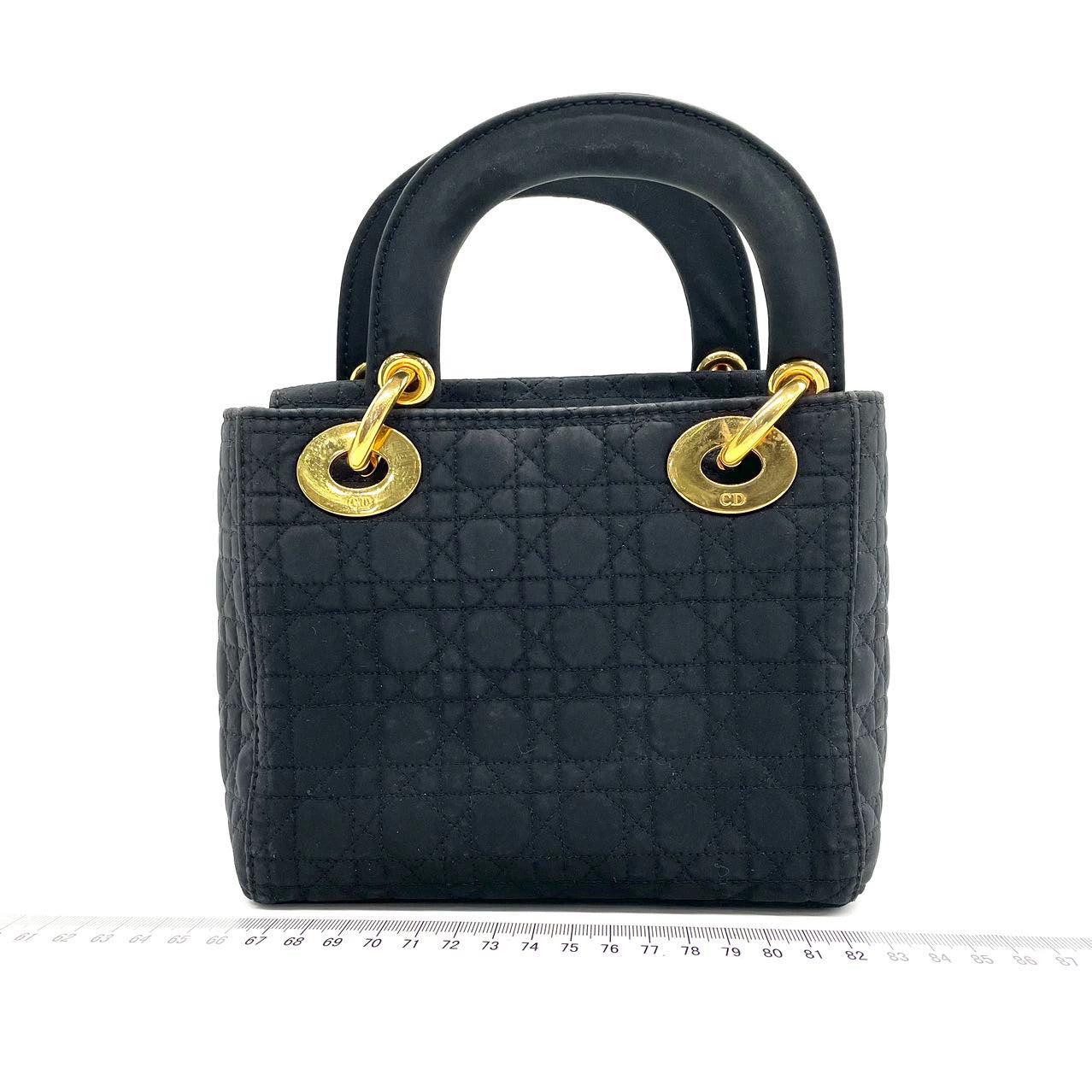 Lady Dior Vintage Mini Black Cloth with Yellow Gold-tone Hardware Dies sind professionelle Fotos der tatsächlichen Tasche angeboten von Luxbags. Diese Mini-Handtasche aus hochwertigem schwarzem Stoff mit den ikonischen Mikronähten ist ein stilvolles