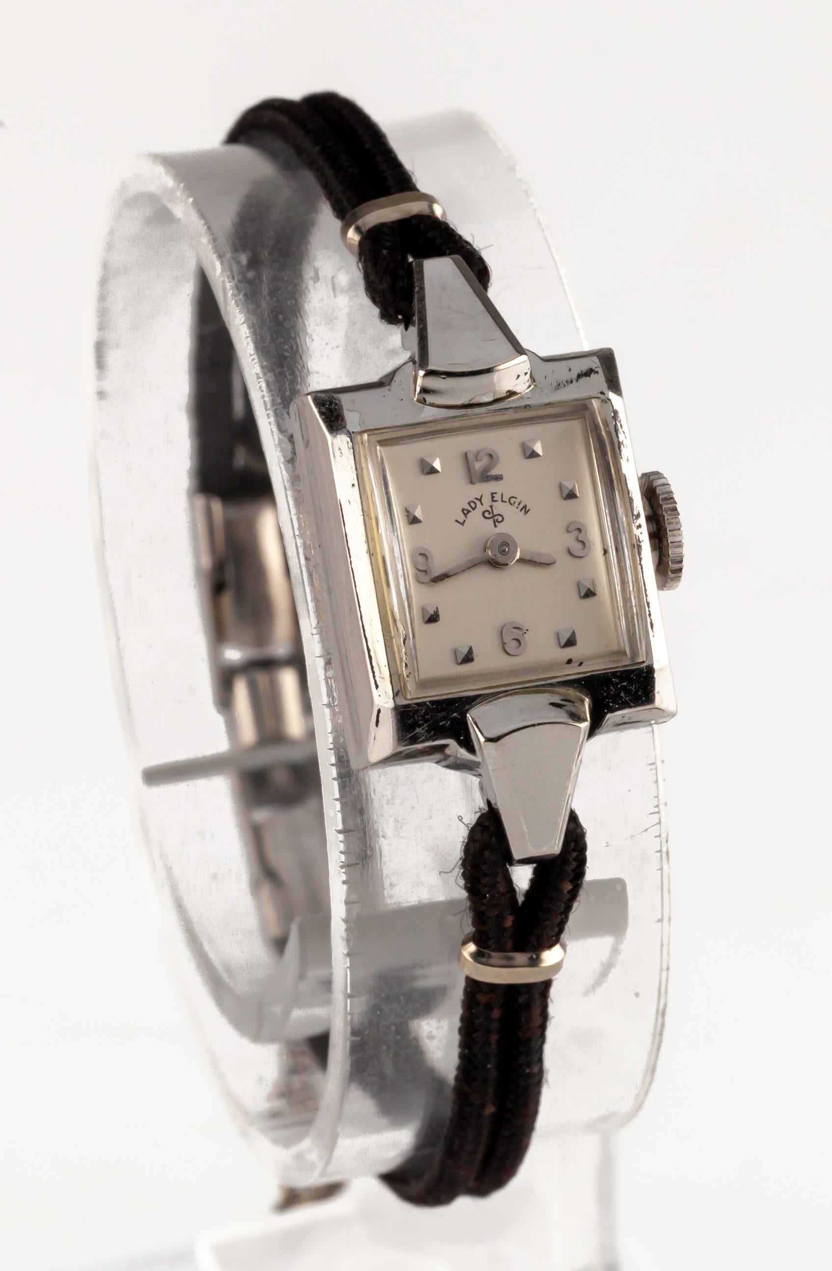 Lady Elgin 14k White Gold Handwinding Wristwatch w/ Cord Band

Movement #650
Movement Serial #F-616923
Case #4246-6659

14k White Gold Square Case
14 mm Wide (16 mm w/ Crown)
17 mm Long

Silver Dial w/ Silver Arabic Numbers, Tic Marks and Hands (M +