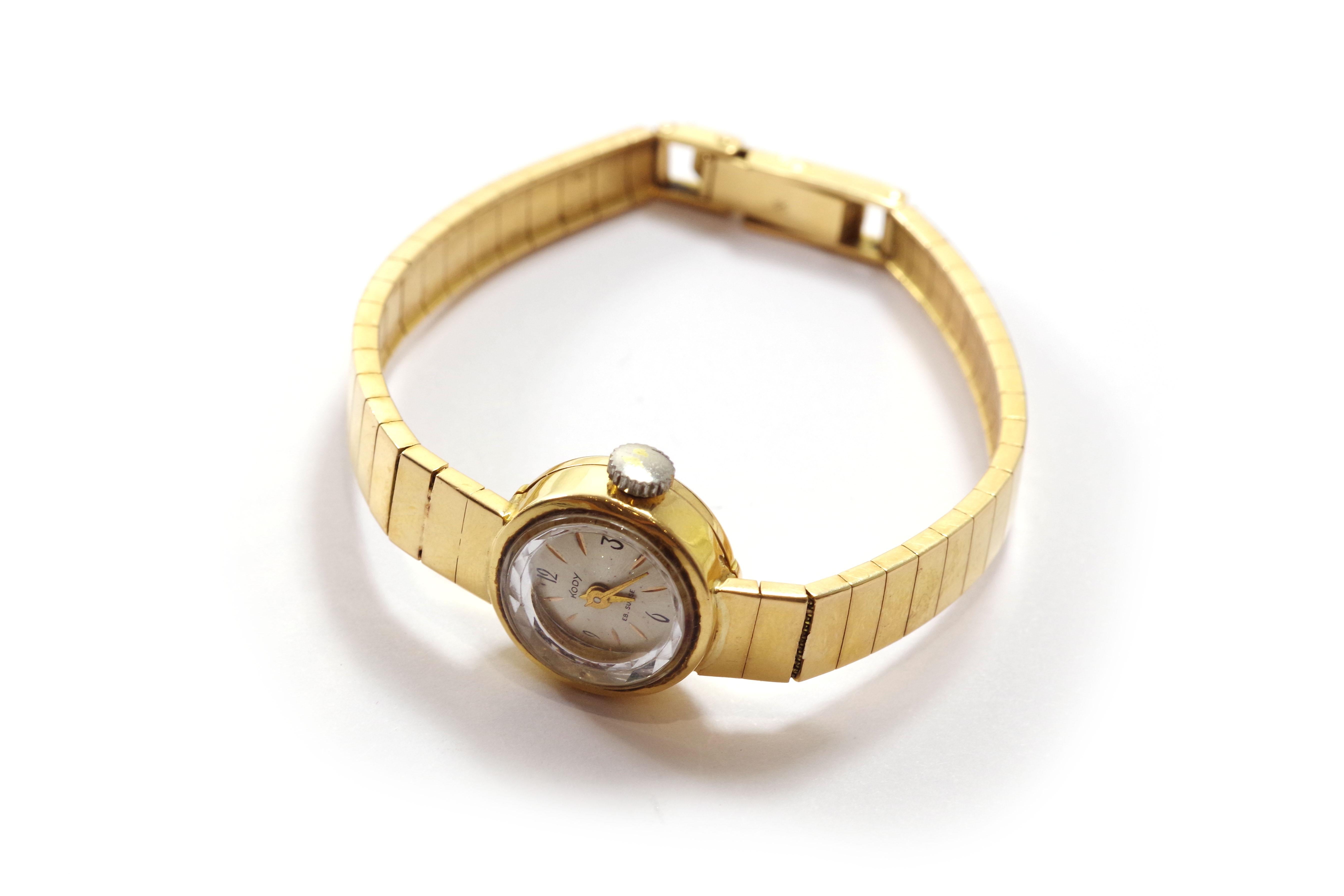 Lady Kody gold watch in 18k yellow gold. This lady's watch features a round case with a bracelet consisting of rectangular articulated links. The dial is cream-colored enamel, and the hands are gold-toned. The movement is a manual winding mechanical