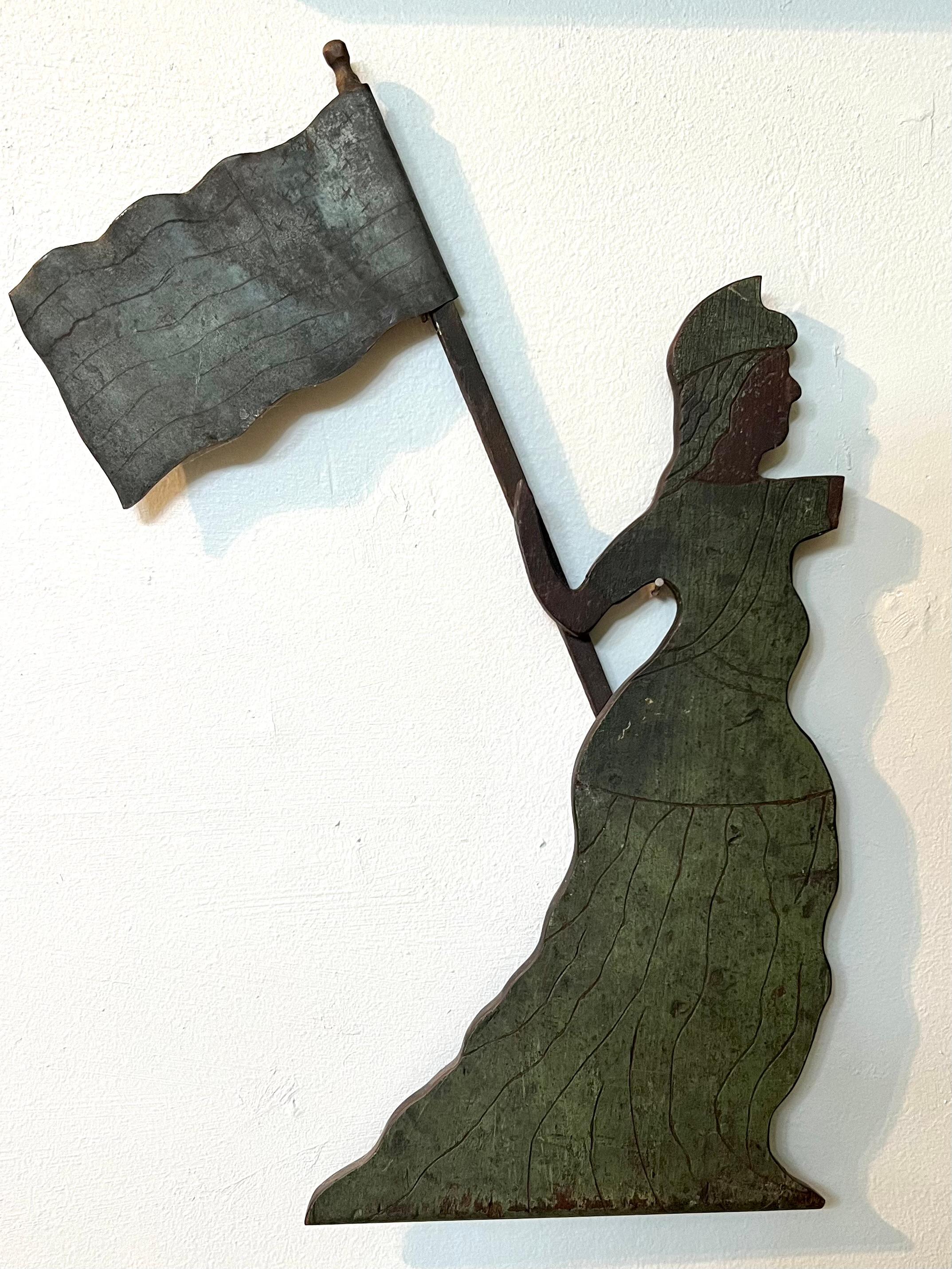 Probably part of a weathervane dating to the late 19th century.  The surface and green patina is excellent, dry and early.  The figure is wood and the flag appears to be tin.  18