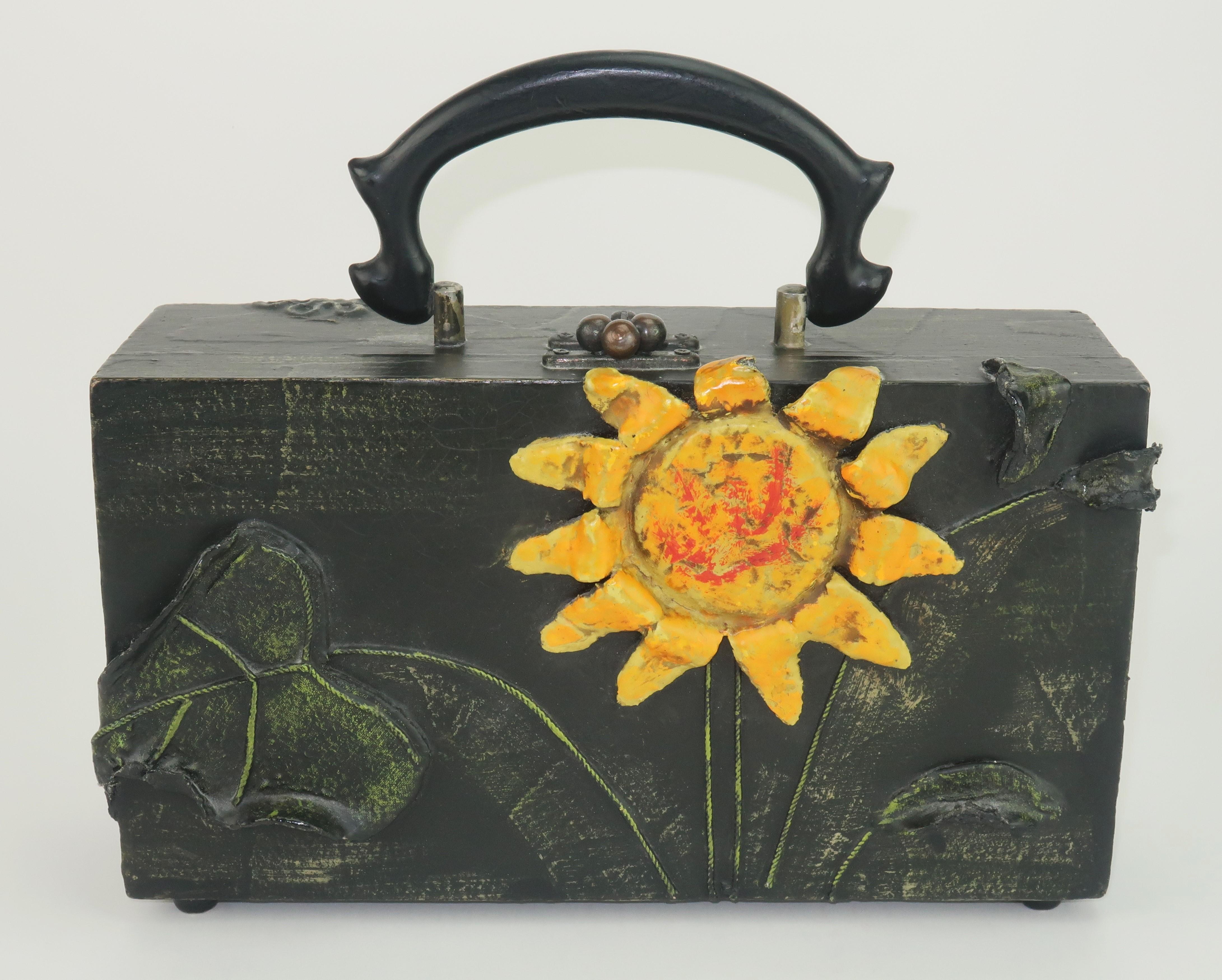 1970 Lady London novelty wood box handbag in a deep dark green (almost black) with fabric and papier mache decoration depicting a yellow sunflower highlighted with a touch of red.  It opens with a door knocker style closure and reveals an orange