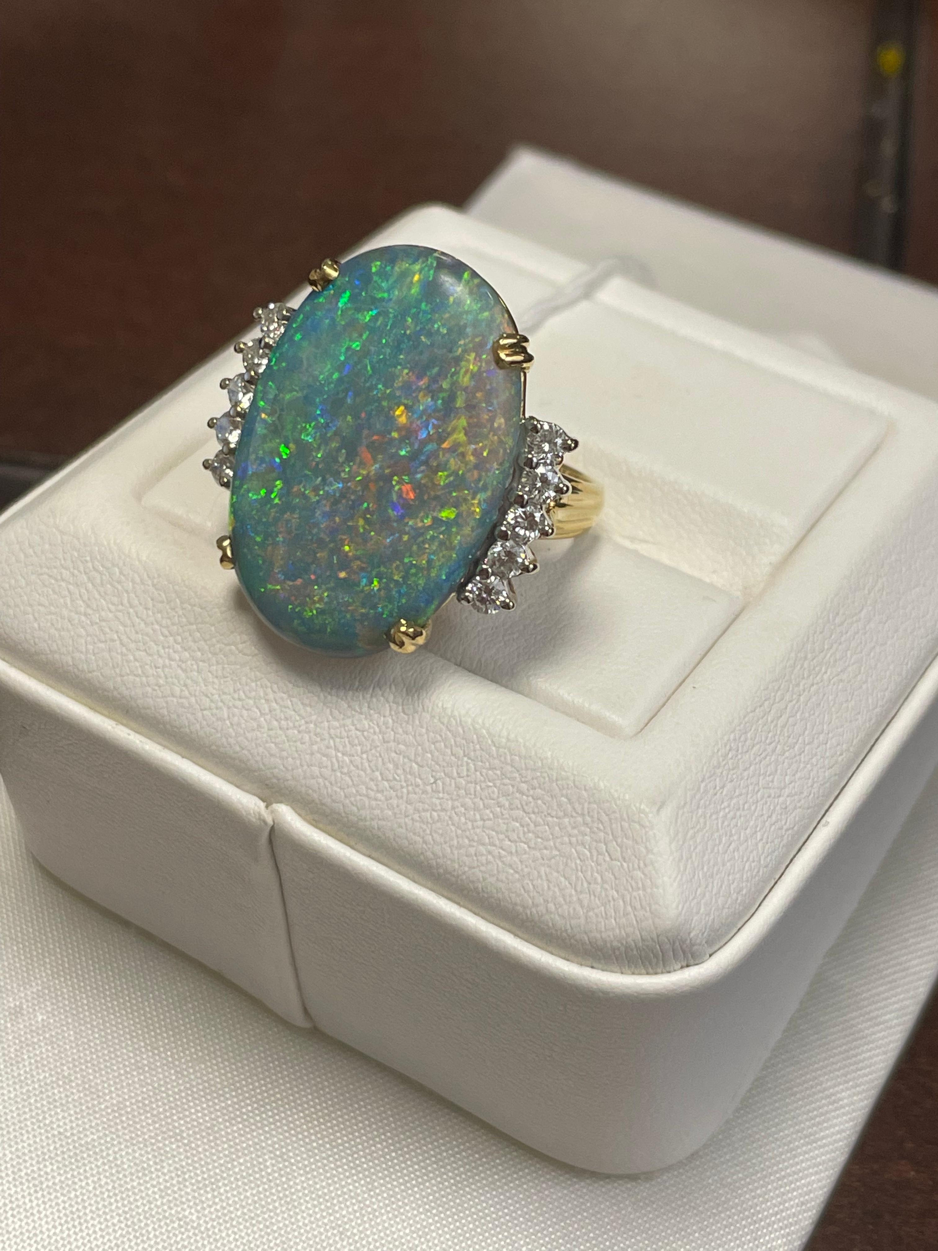 L'opale semi-noire d'une dame avec une couleur de feu bleu-vert, jaune et orange. L'échelle de saturation est moyenne avec un motif de feu d'artifice.  Brillant, en forme de cabochon mesurant 26 x 18,6 mm et pesant 15,0 carats.  10 diamants ronds de