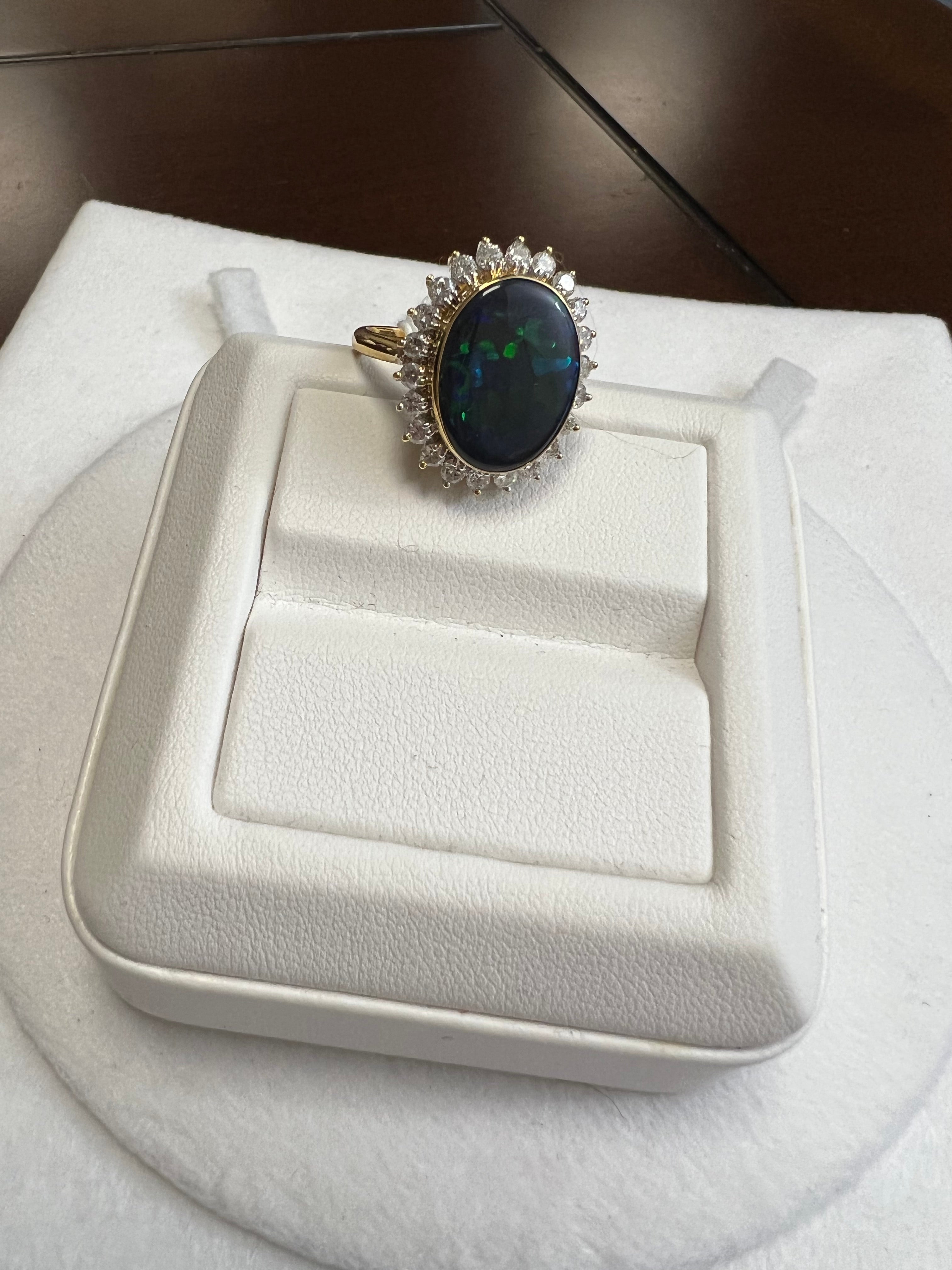One lady's black opal in blue-green fire color. Average saturation scale with a flash fire pattern. Brightness of fire is very bright with cabochon, oval shape. Weight is 7.50 carats. 22 round brilliant cut diamond measuring 2.2 mm. Total weight is