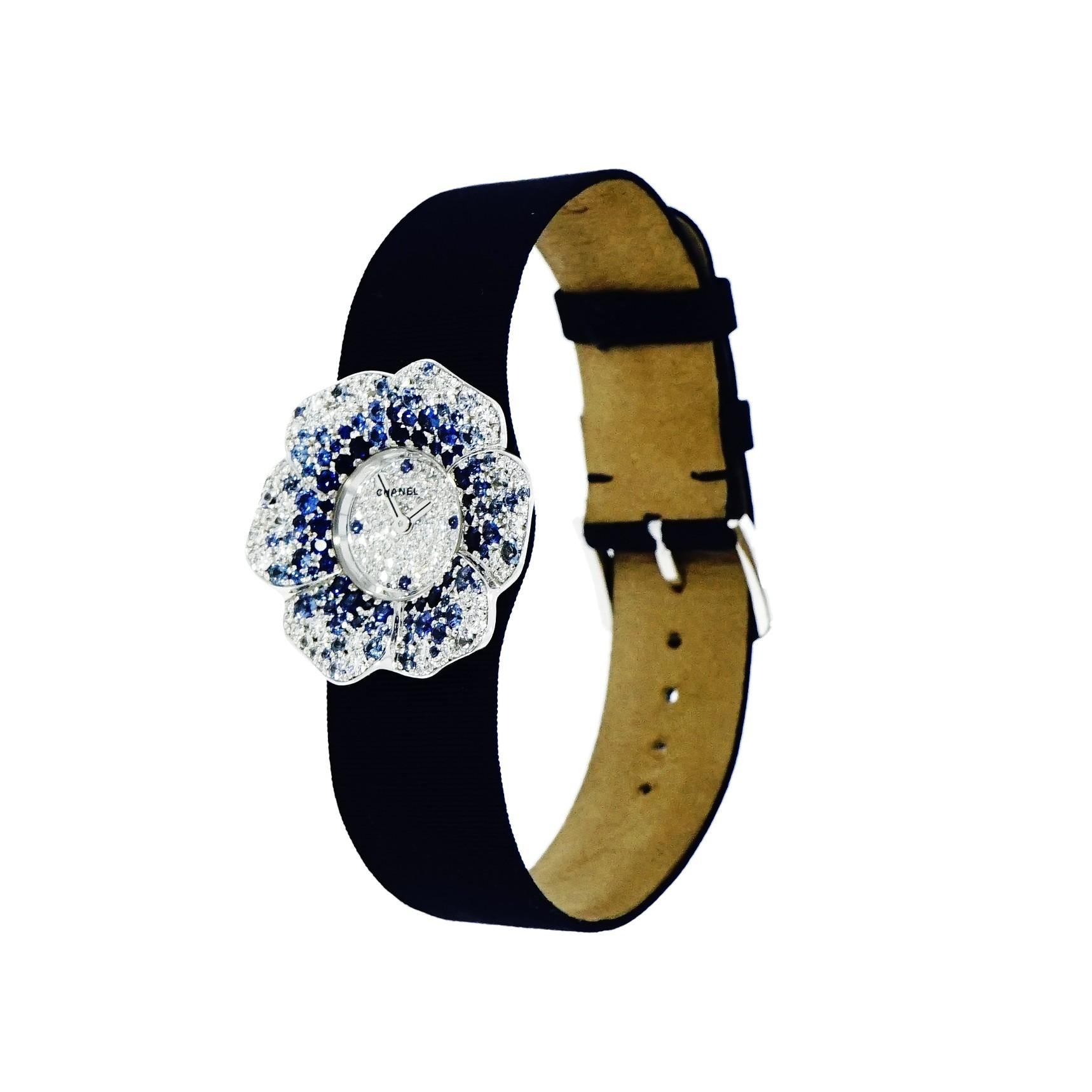 Pre-owned in very good condition Lady’s Chanel Camelia 27mm white gold case set with diamonds and graduated color blue sapphires, quartz movement, pave diamond dial with 12,3,6,9 blue sapphire hour markers, blue satin strap with white gold tang