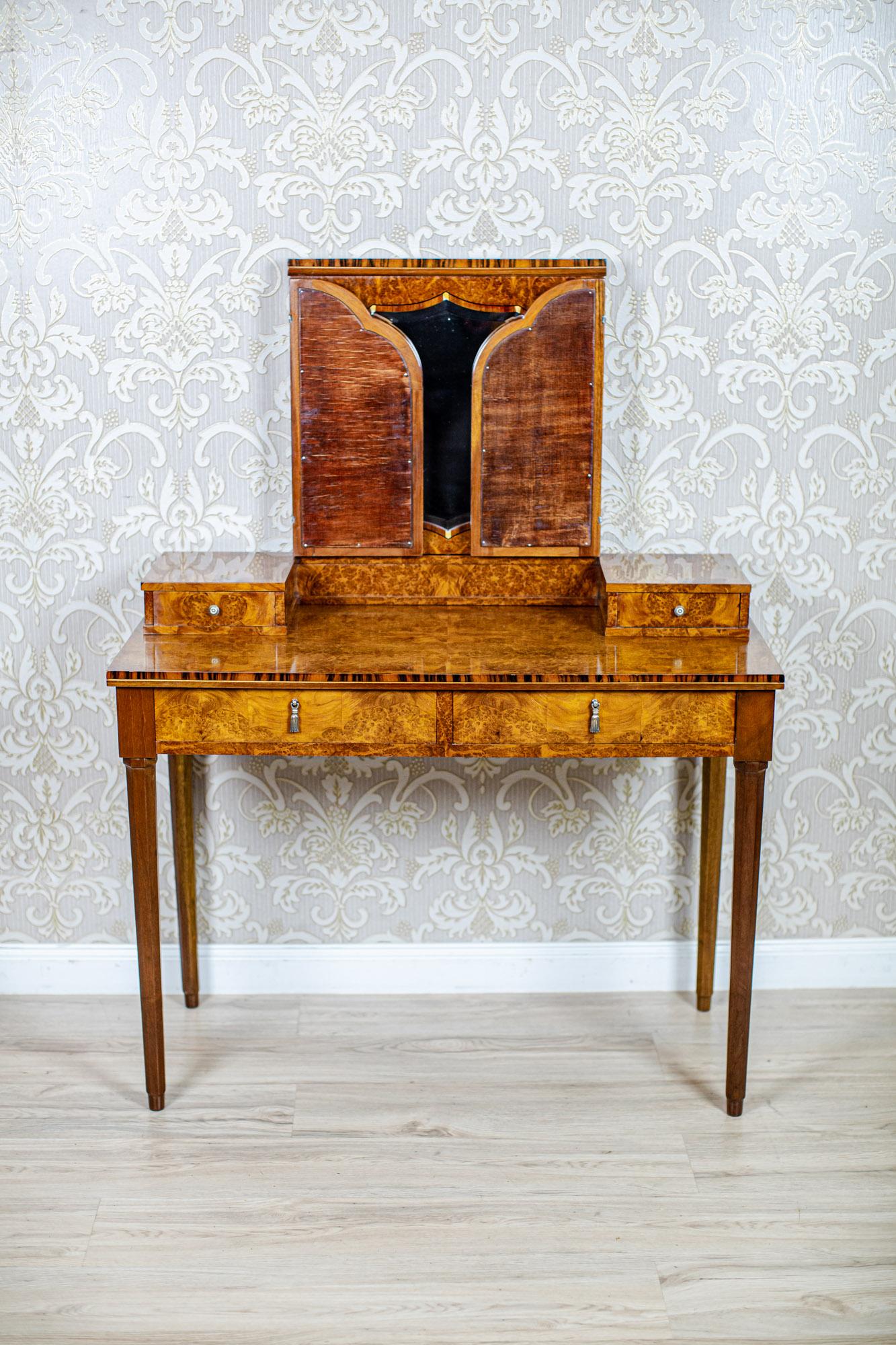Lady's Vanity Table From the Early 20th Century

An Art Deco piece of furniture on high, straight legs, with drawers in the corpus.
The add-on unit is composed of an inlaid frame with a mirror, which is flanked by two smaller mirrors.
The whole is